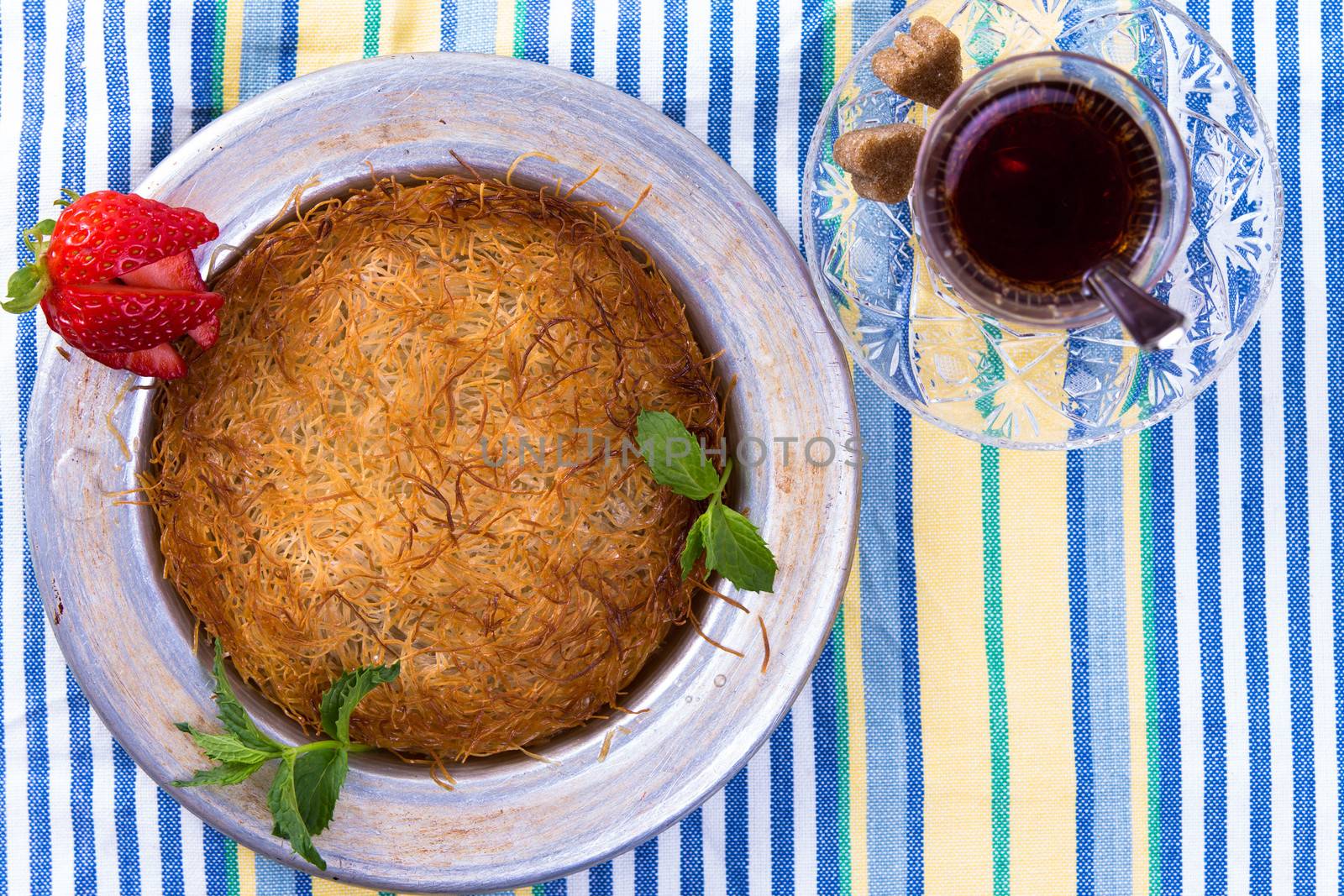 Turkish dessert kunefe on a picnic cloth with mints and sliced strawberry along with Turkish hot tea