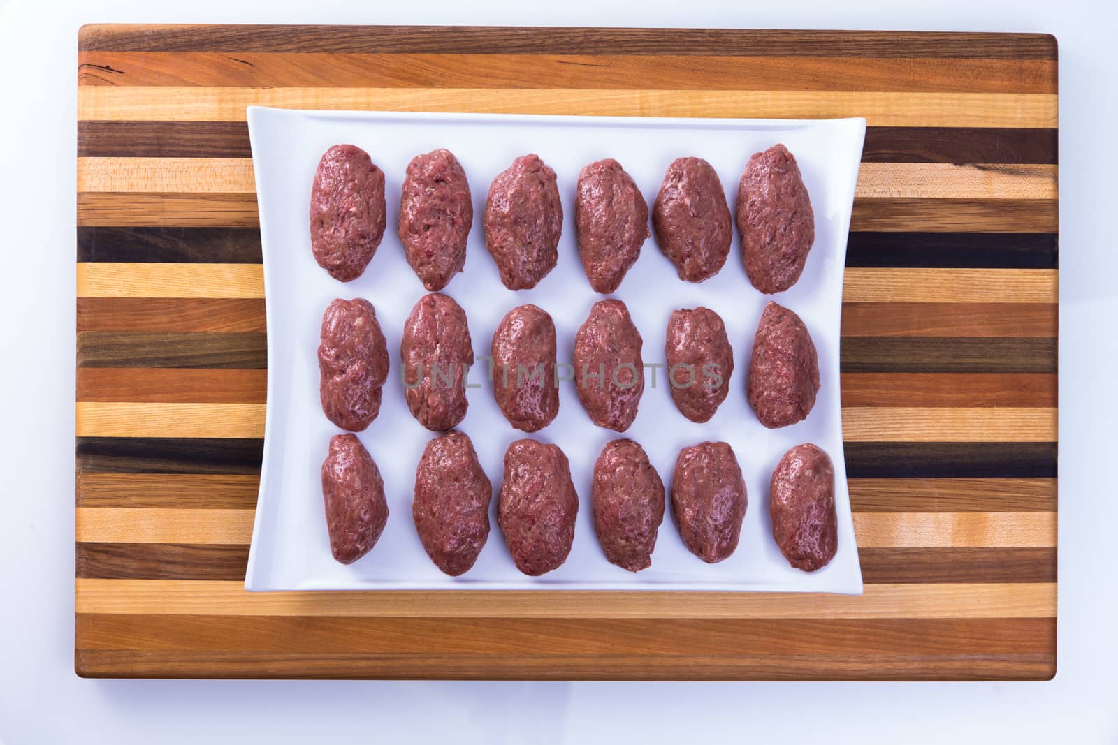Hand rolled Turkish meat balls on a white plate lined up and ready to cook in a white plate on multicolor curring board