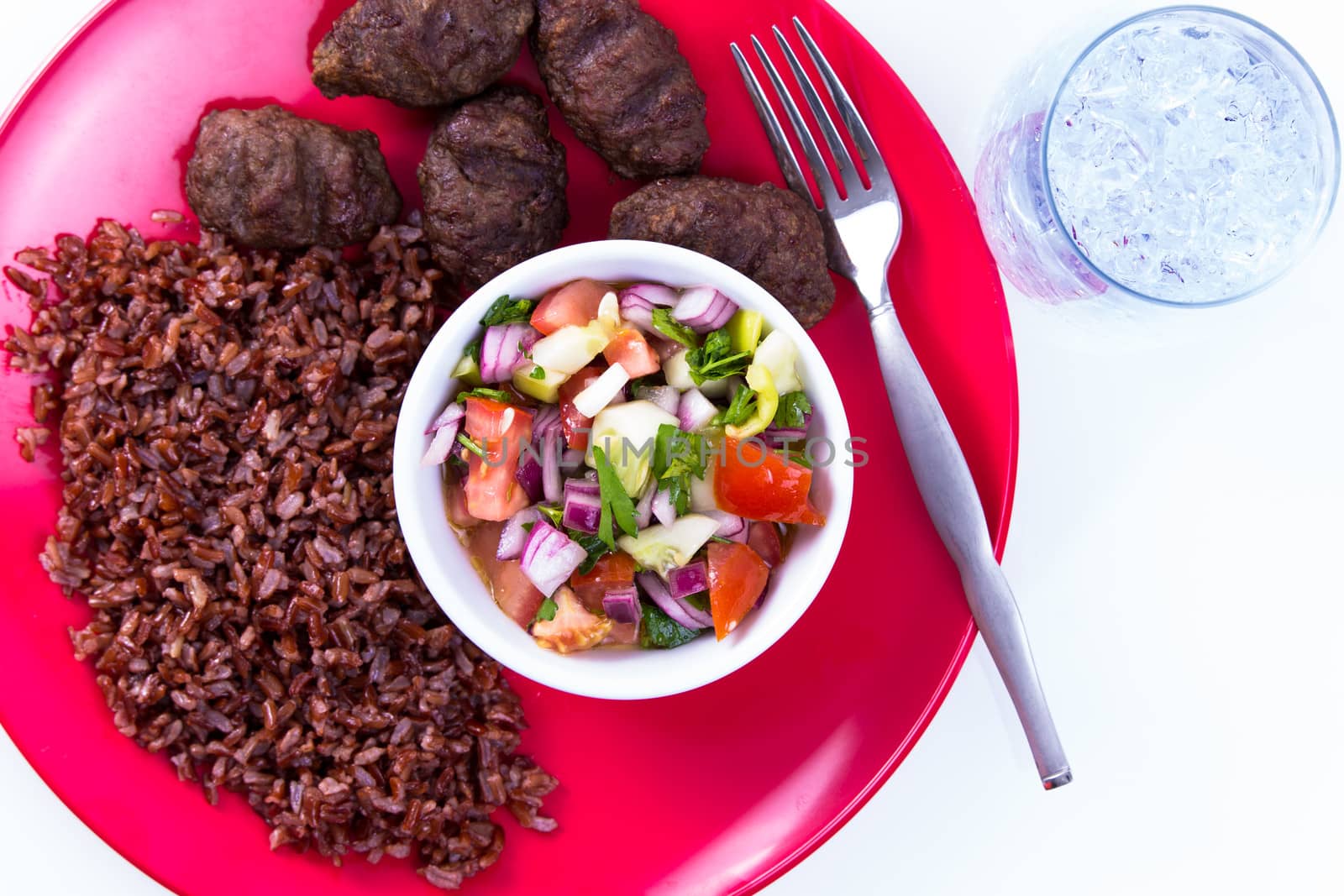 Turkish Meat Balls Kofte served with Red Rice Pilaf and Turkish Shepperd Salad on a red plate along with ice water. Isolated on white