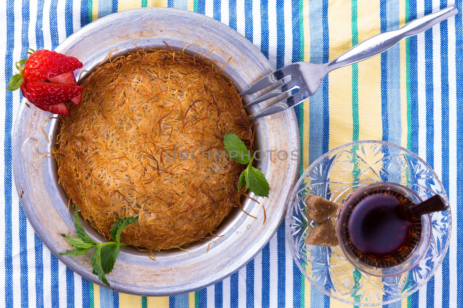 Turkish dessert kunefe isolated on a picnic cloth with mints and sliced strawberry along with Turkish hot tea