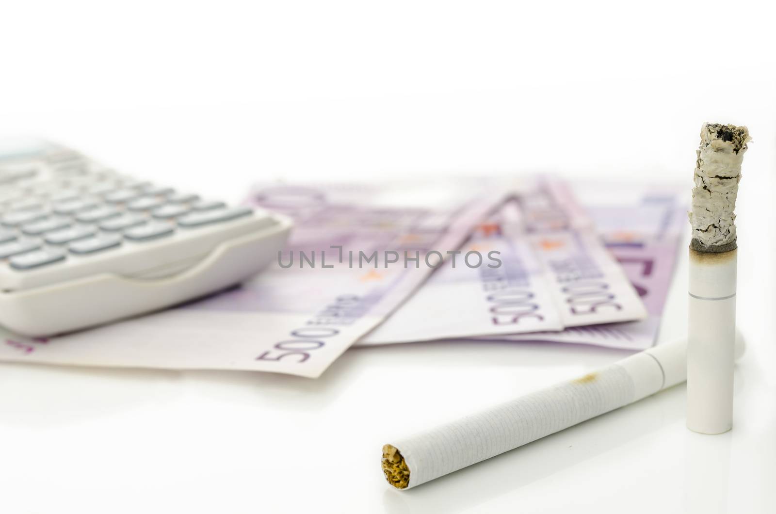 Half burned cigarette with Euro money and calculator in background. Concept of expensive habit.