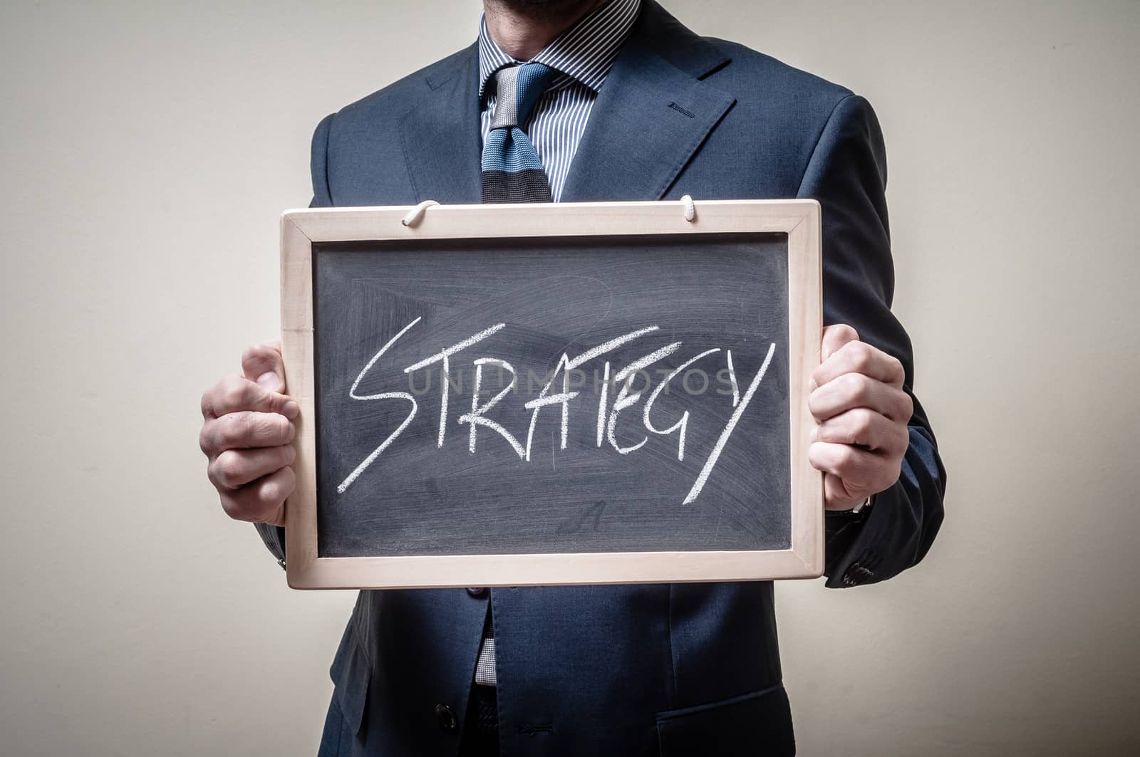 businessman holding blackboard written strategy on gray background