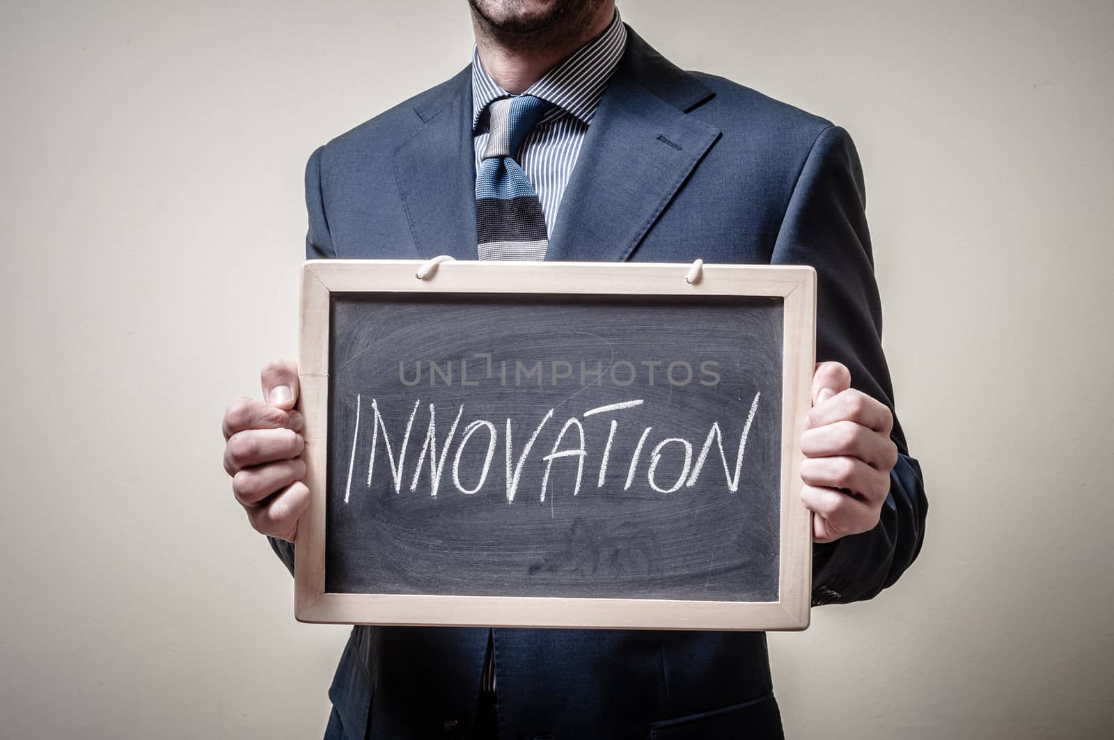 businessman holding blackboard written innovation on gray background