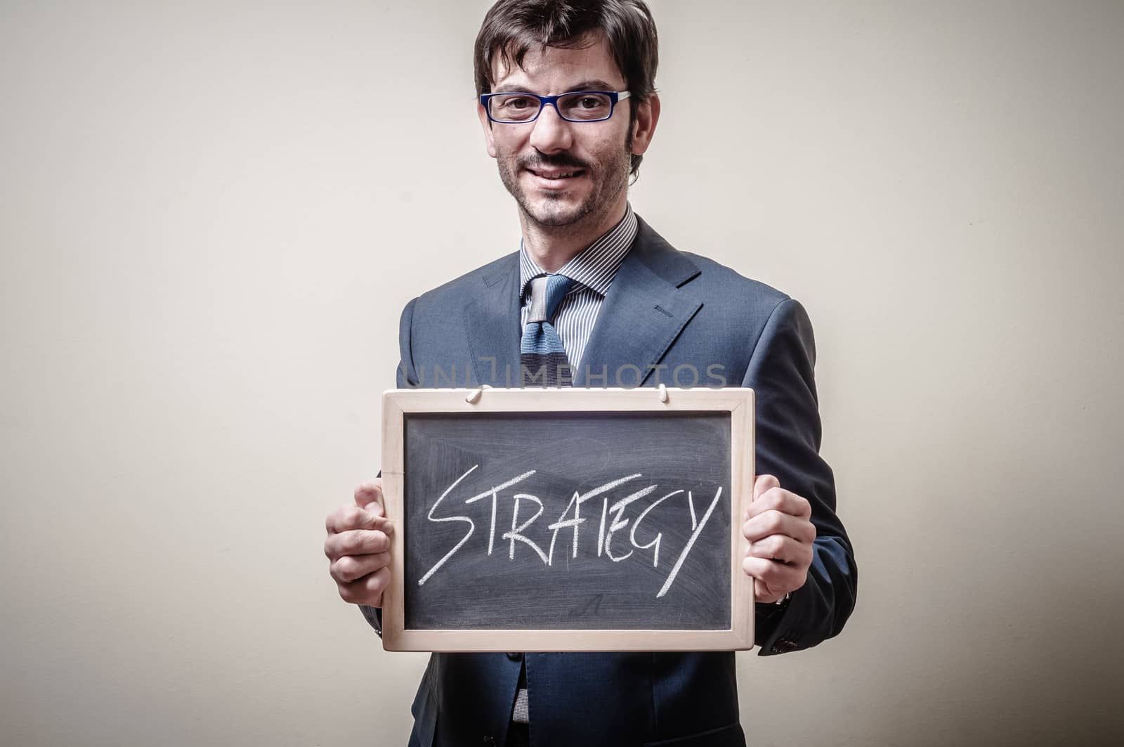 businessman holding blackboard written strategy on gray background