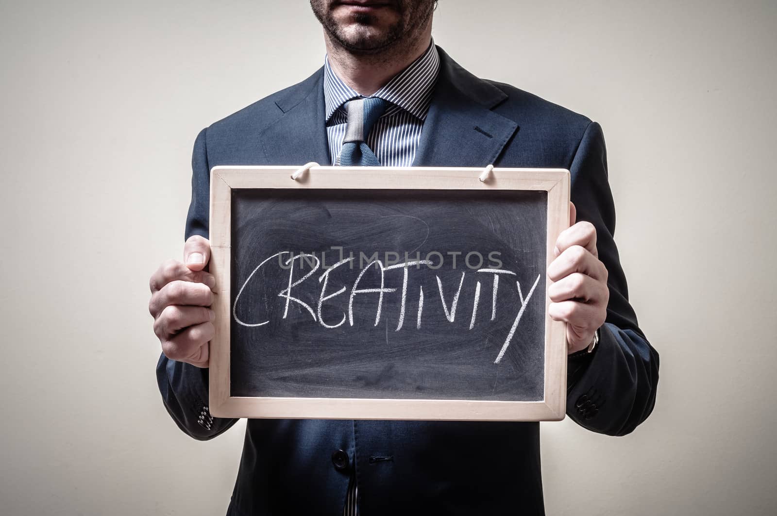 businessman holding blackboard written creativity on gray background