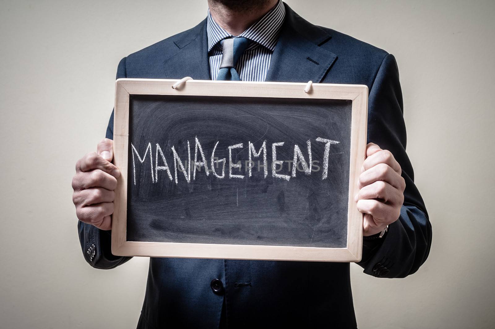 businessman holding blackboard written management on gray background