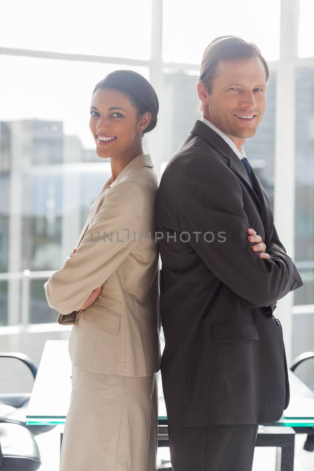 Smiling business people standing back to back in an office