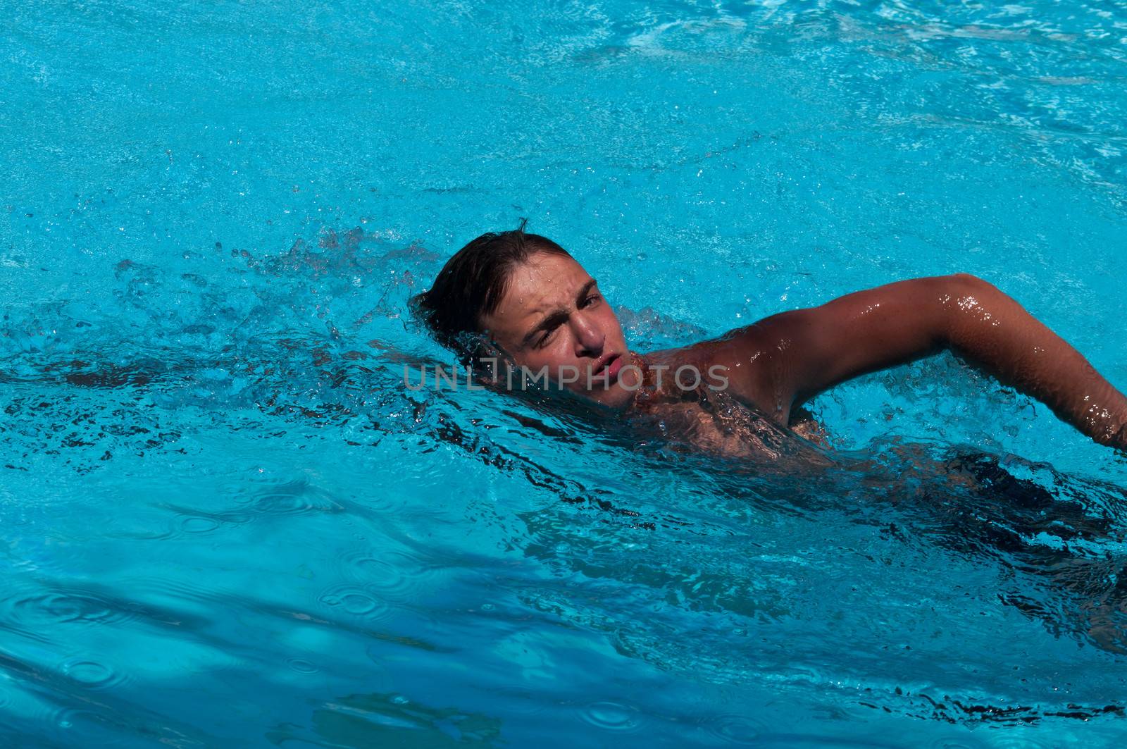 Handsome teenager swims in pool .