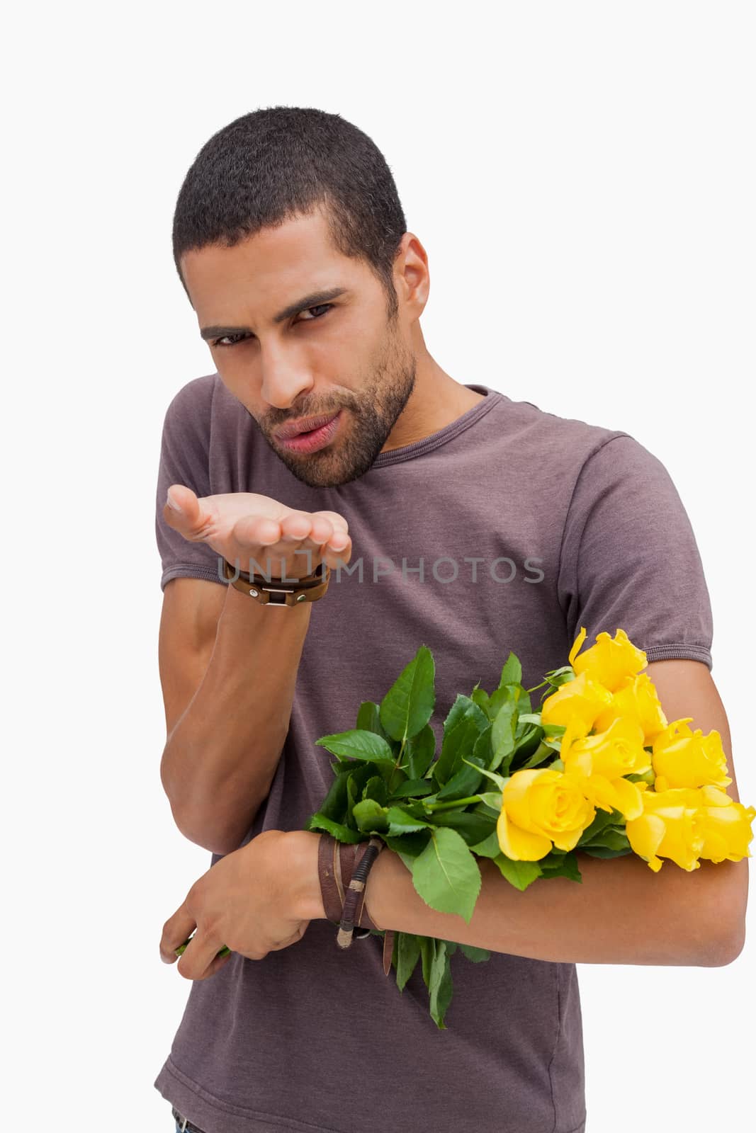 Handsome man blowing a kiss and holding yellow roses on white background