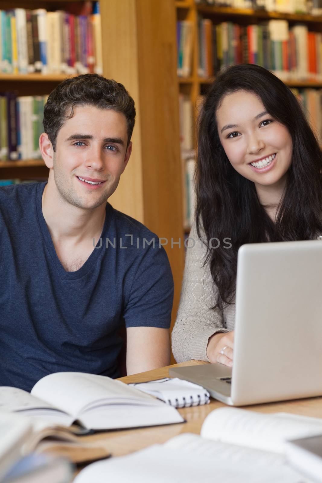 Two students learning with a laptop in a library by Wavebreakmedia