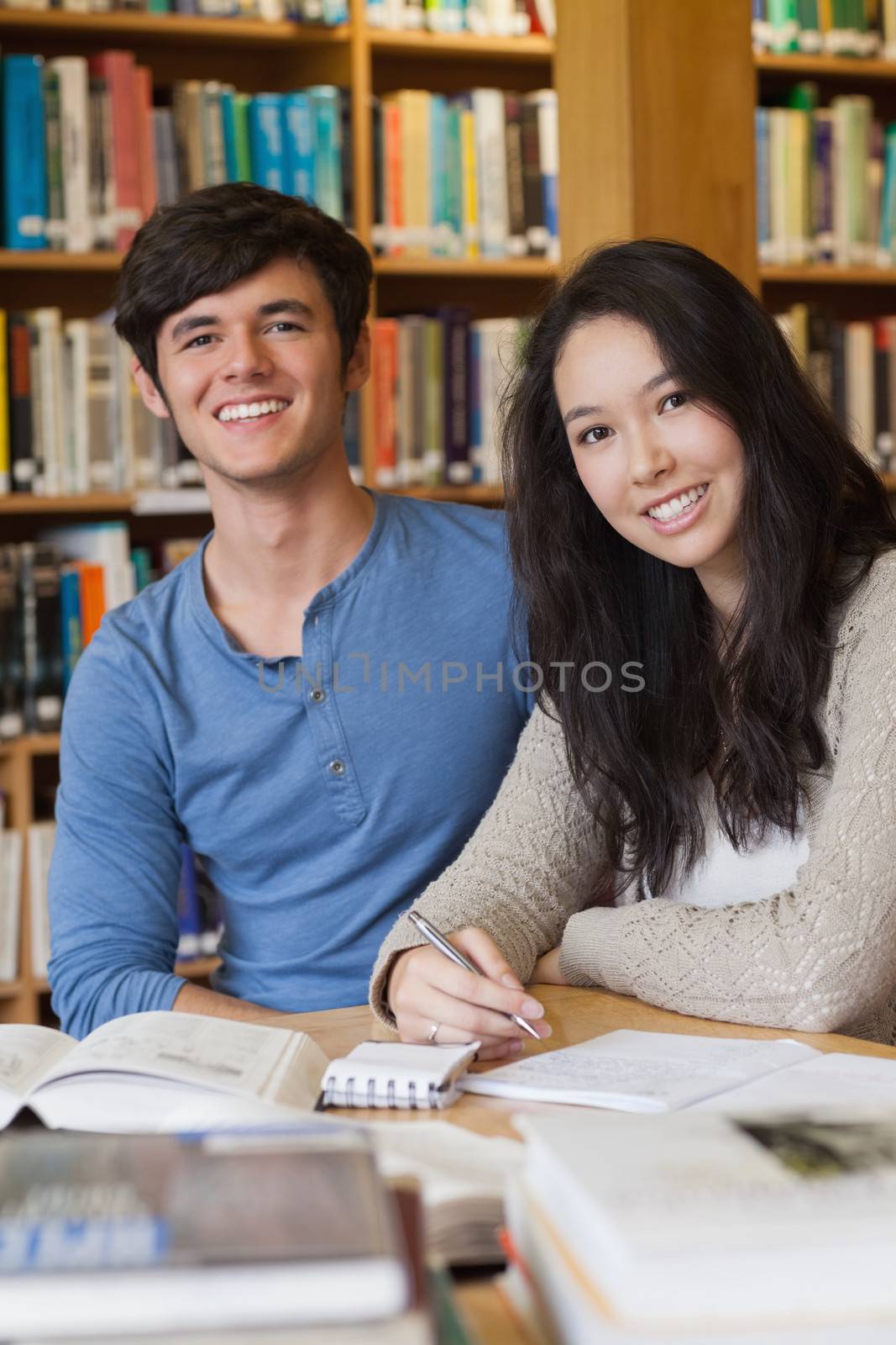 Two people sitting in a library at a desk and learning while smiling