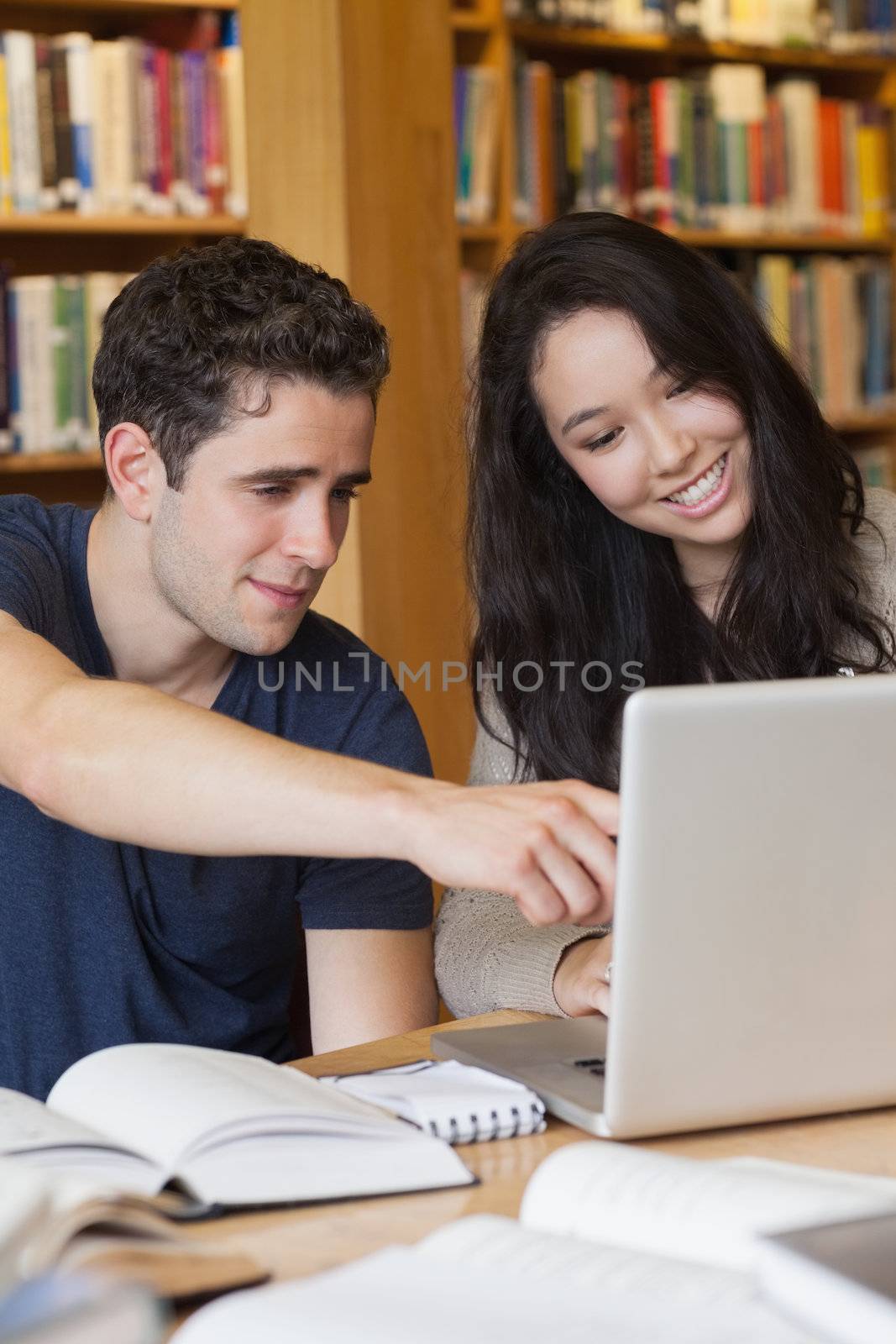 Two students learning on the laptop in a library by Wavebreakmedia
