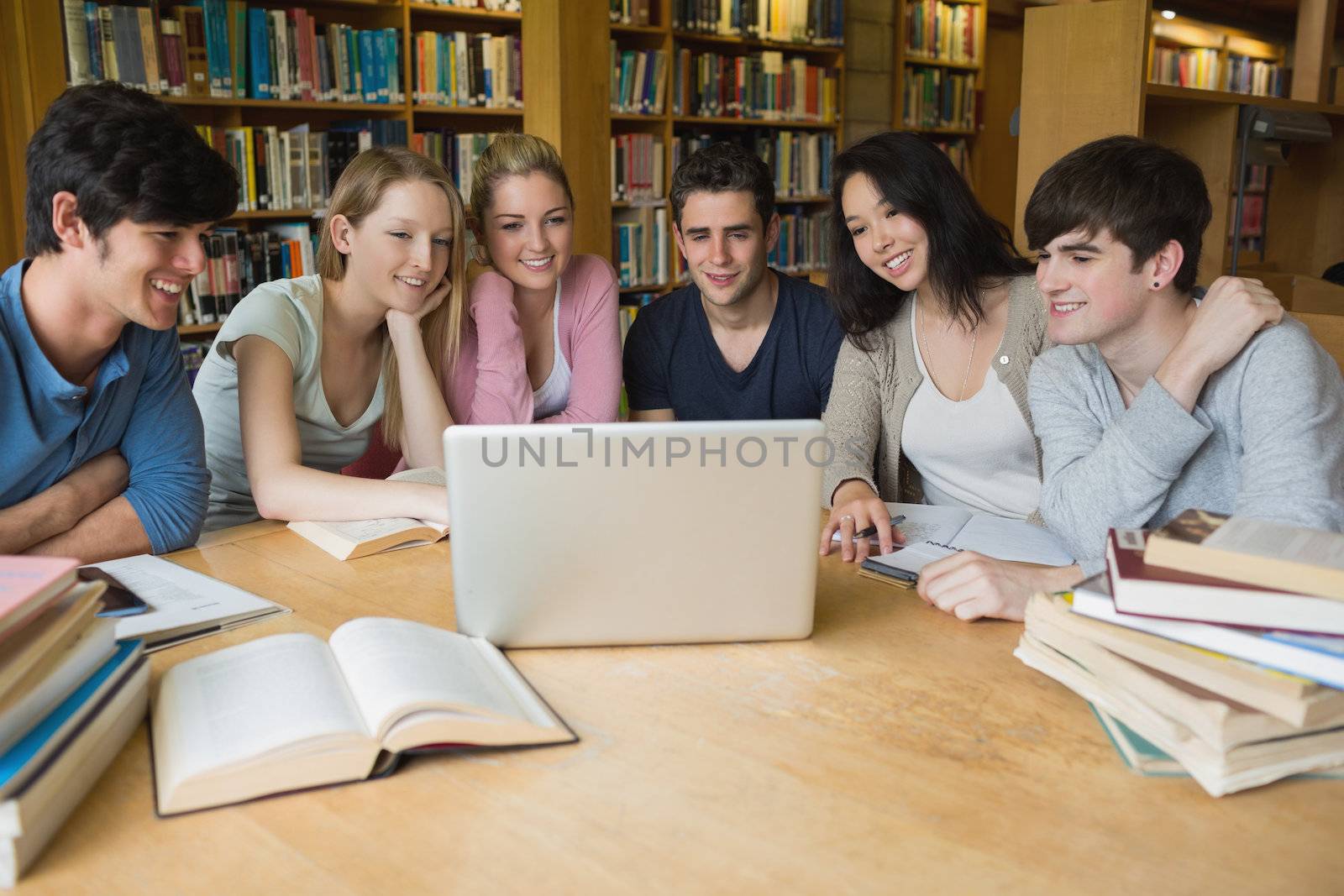 Group of students sitting at a table in a library while learning and using the laptop