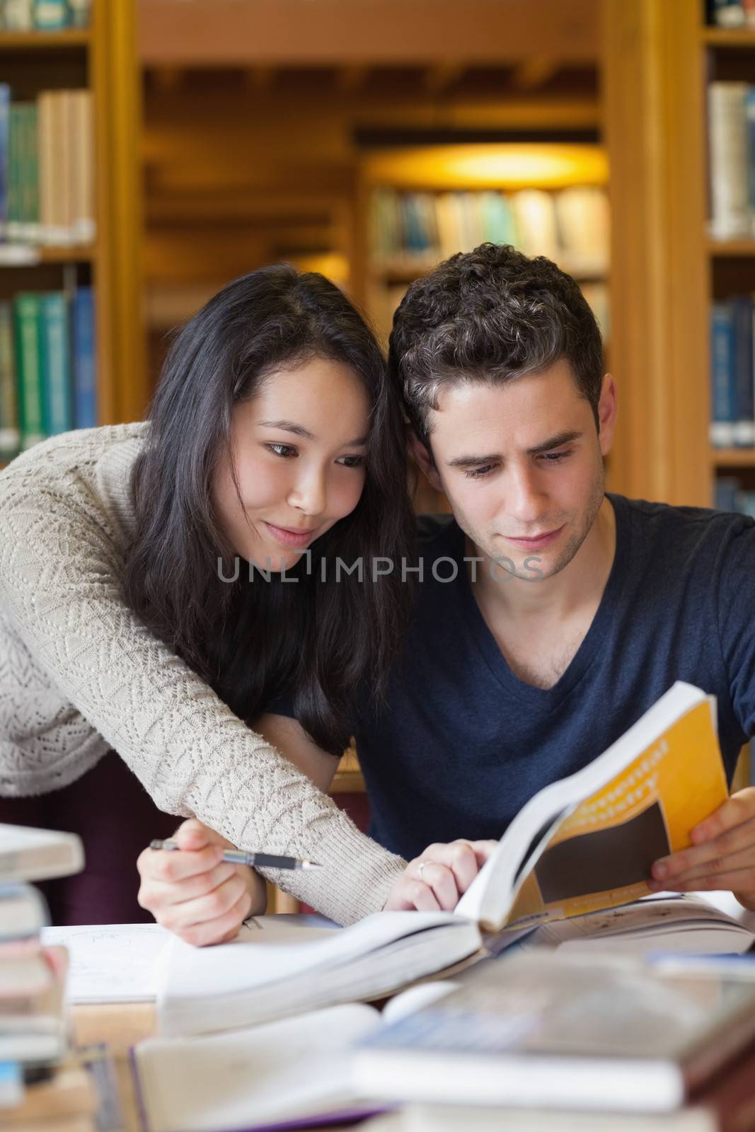 Two students at a table in a library learning and helping each other