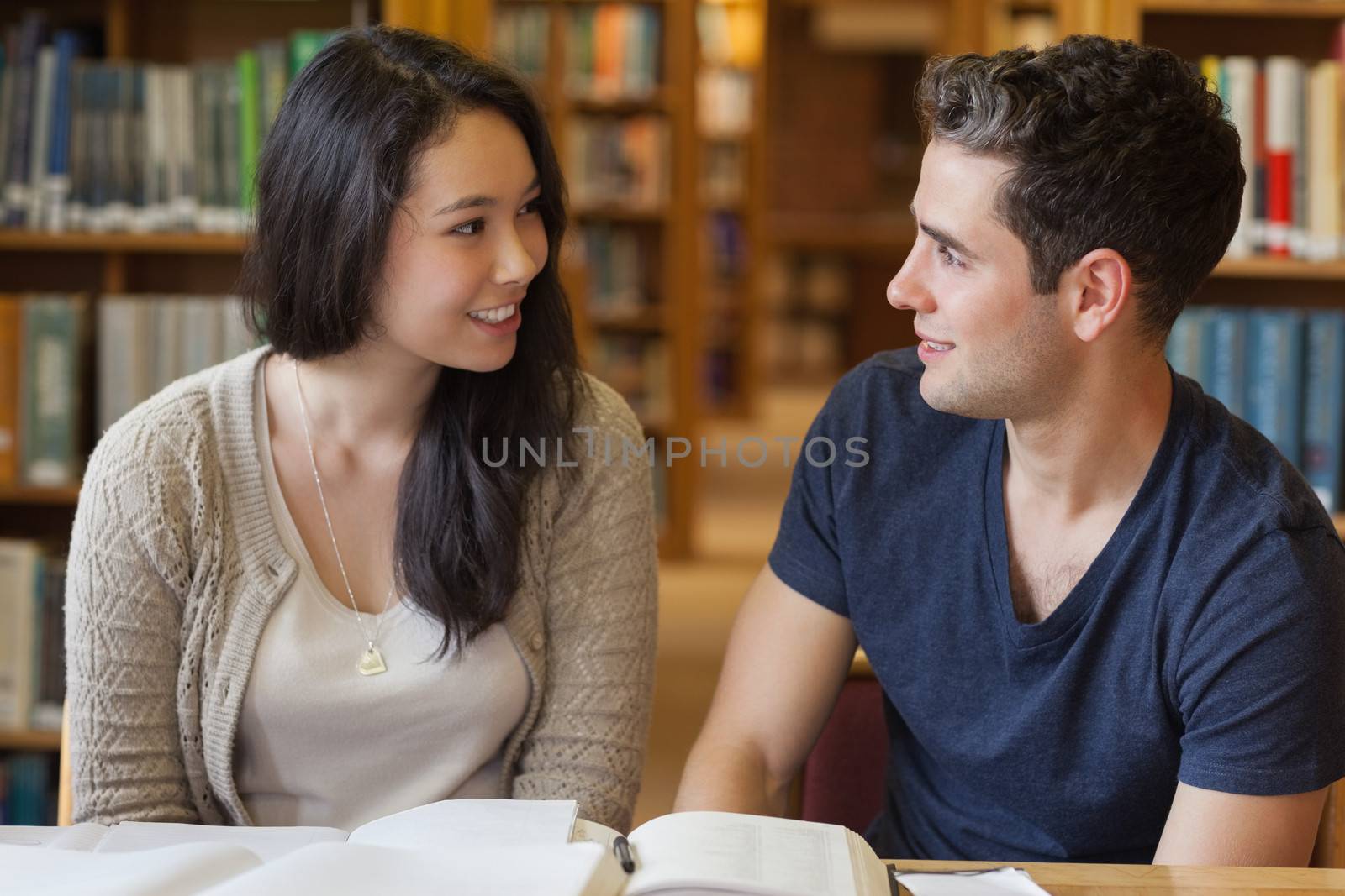 Two students studying while sitting at a desk in a library and talking