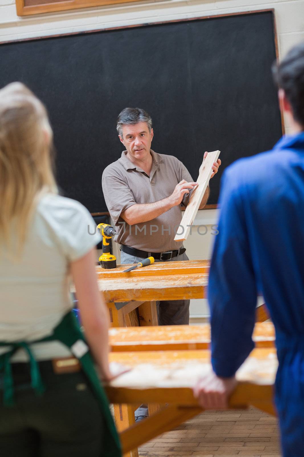 Teacher holding a wooden board while explaining something to his class