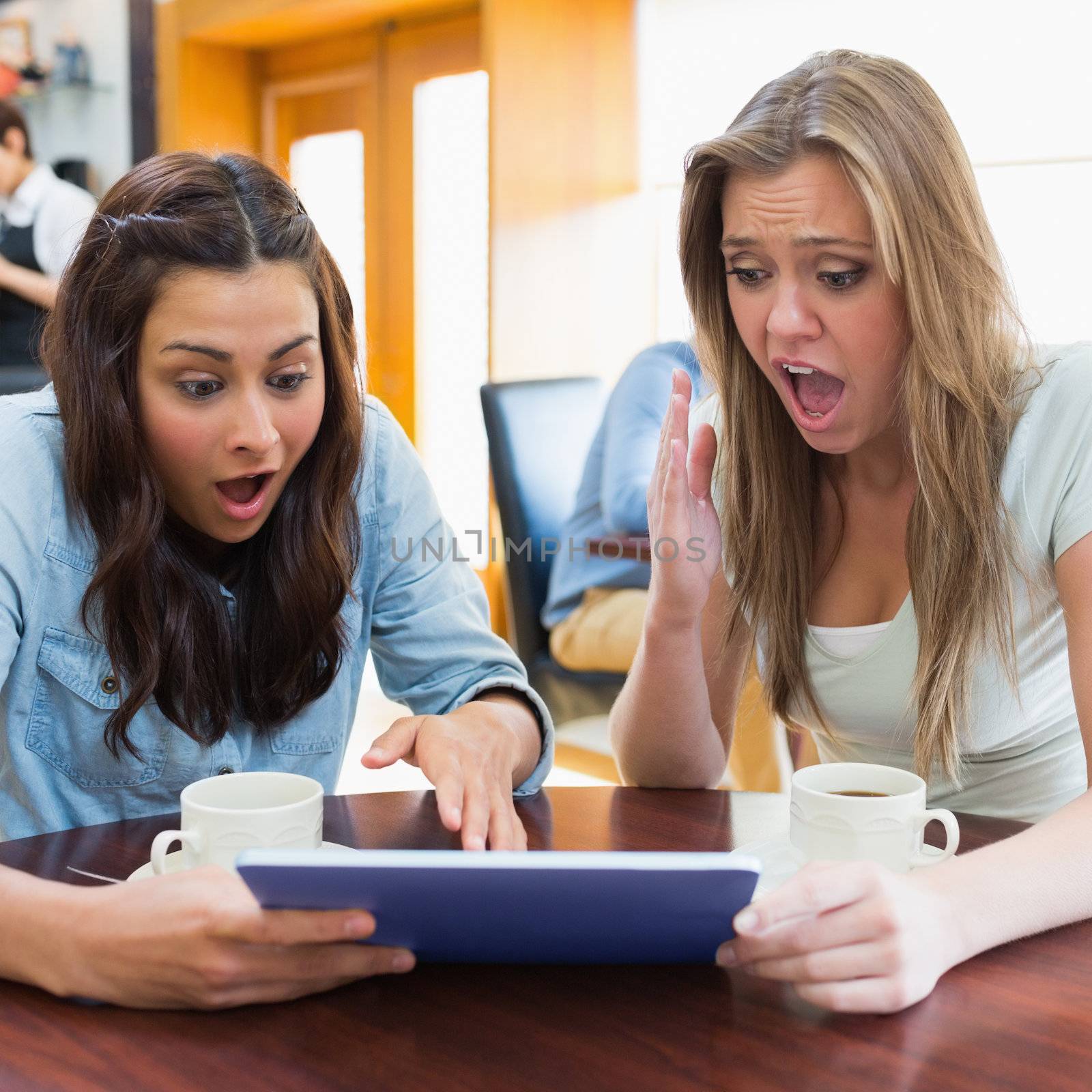 Women looking shocked at tablet pc in canteen by Wavebreakmedia