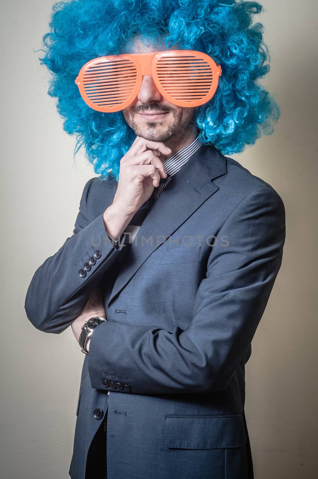 funny businessman with big orange glasses and blue wig on gray background