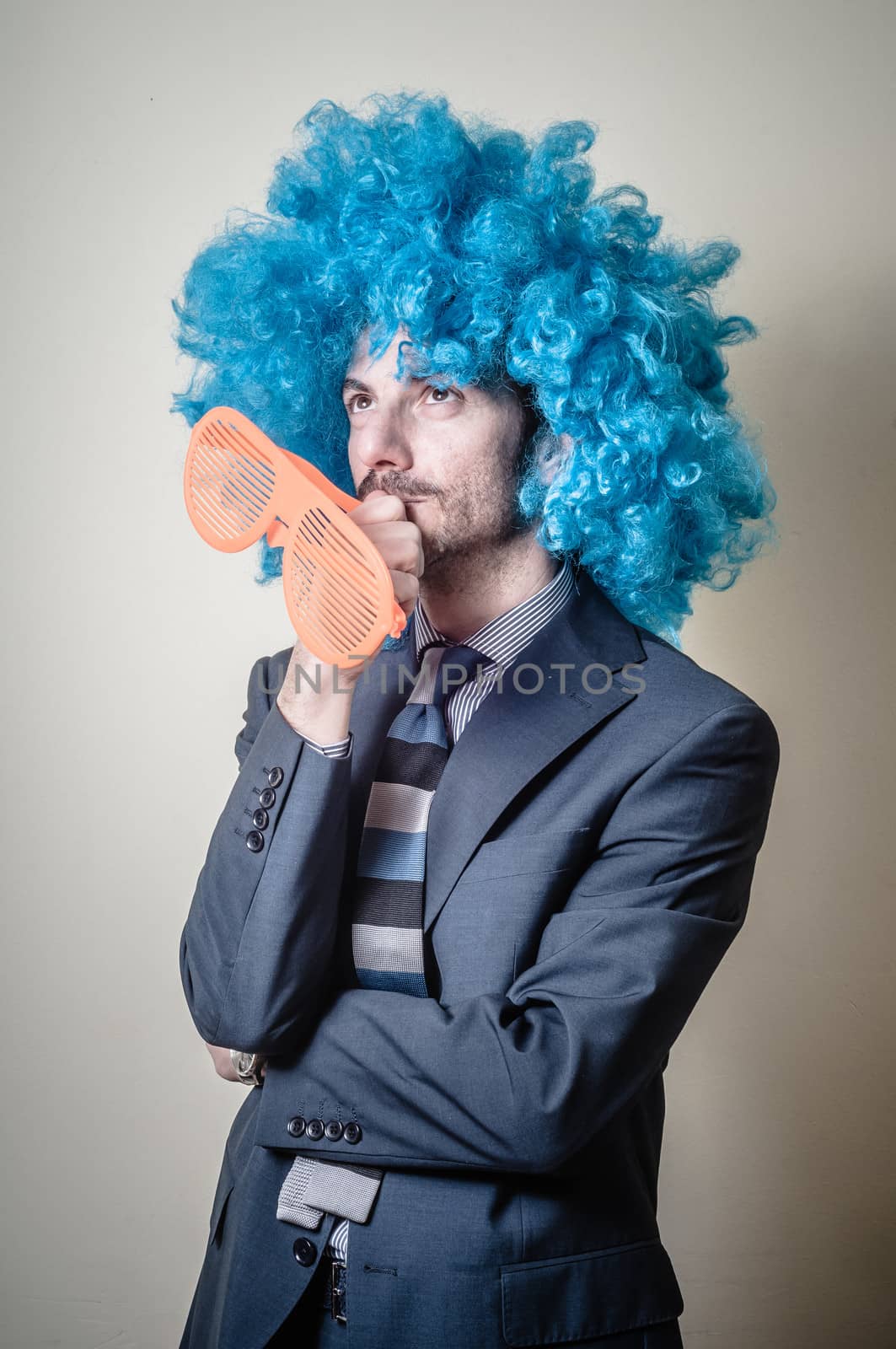 funny businessman with big orange glasses and blue wig on gray background