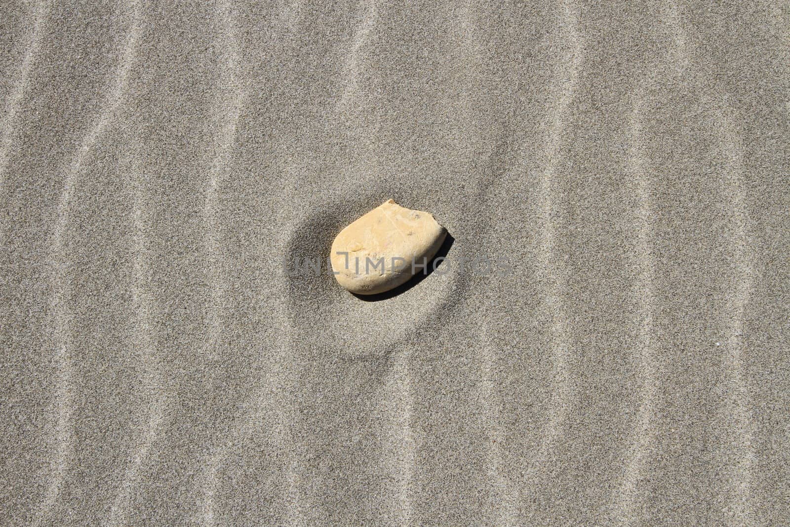 Stone alone in the middle of beach sand waves