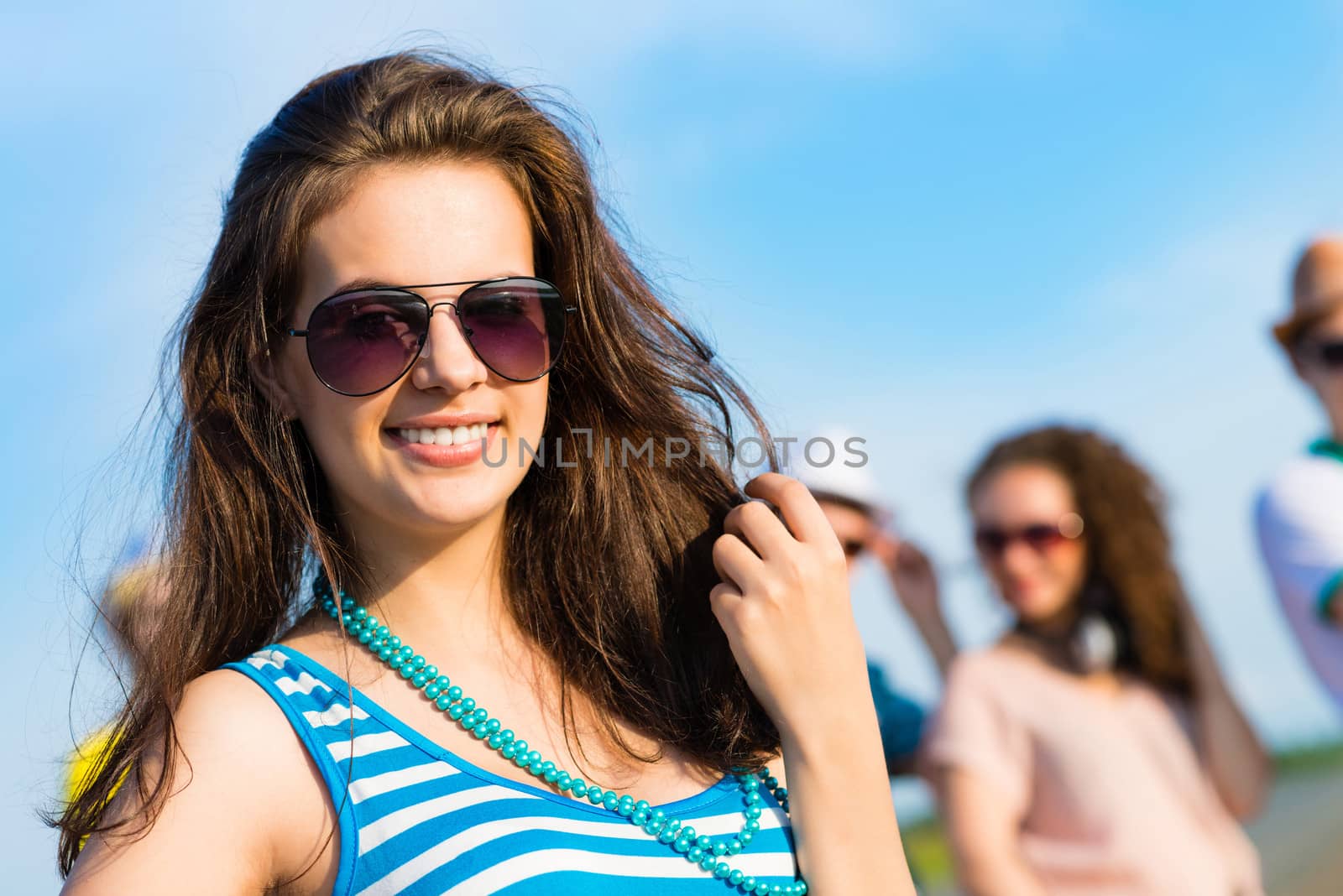 stylish young woman in sunglasses on the background of blue sky and friends