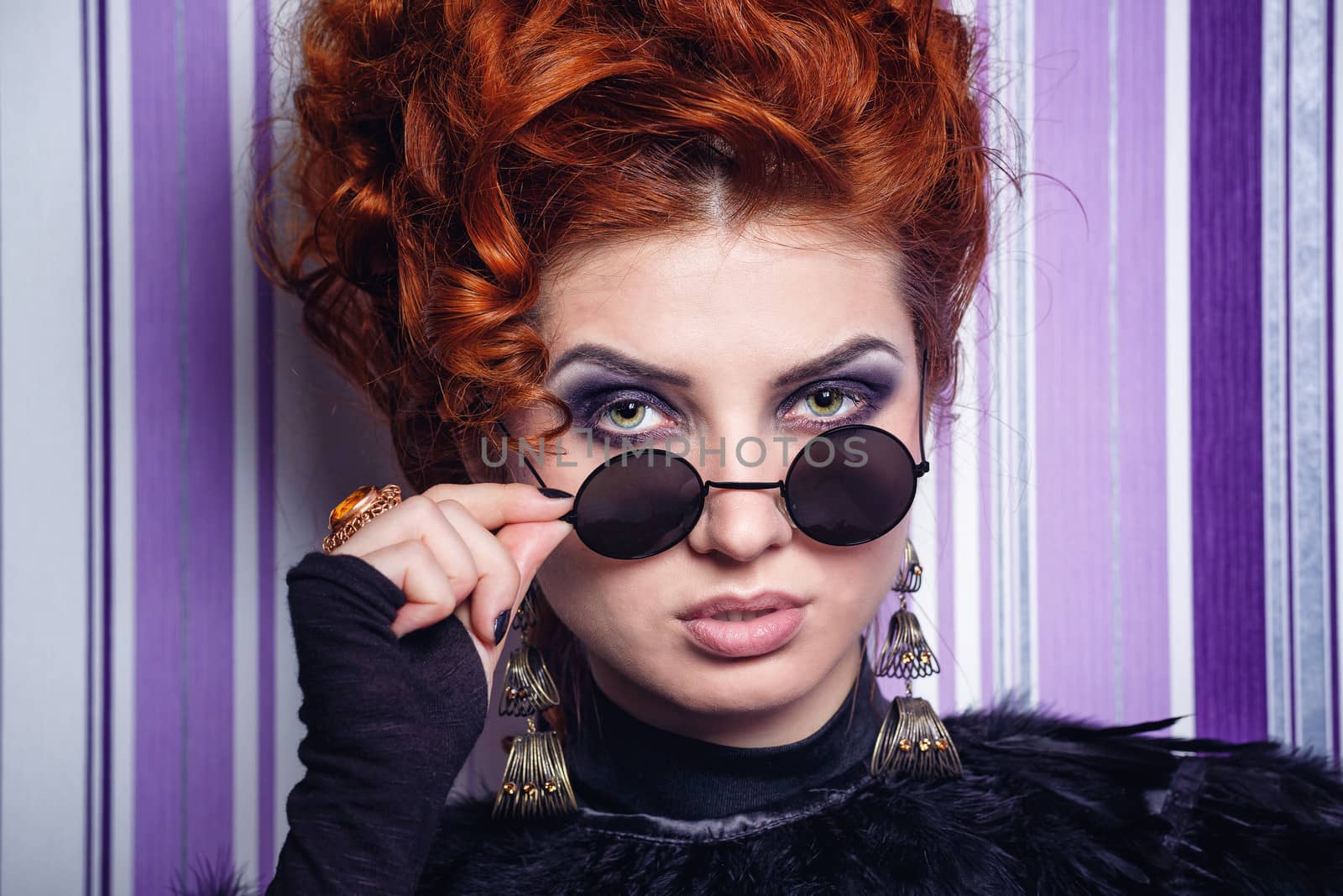 Red-haired girl with makeup looking over sunglasses photographed close-up