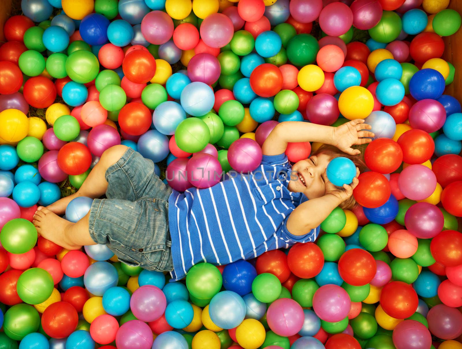 Happy child playing with colorful plastic balls by haveseen