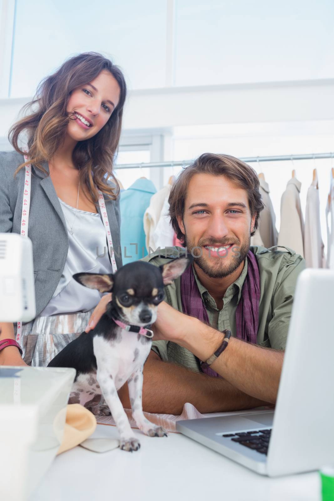 Two fashion designers smiling to the camera with a chihuahua