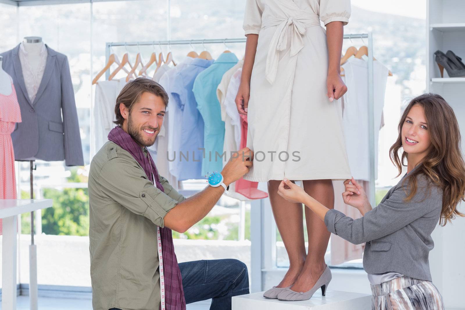 Fashion designers sitting next to a model and working on a dress