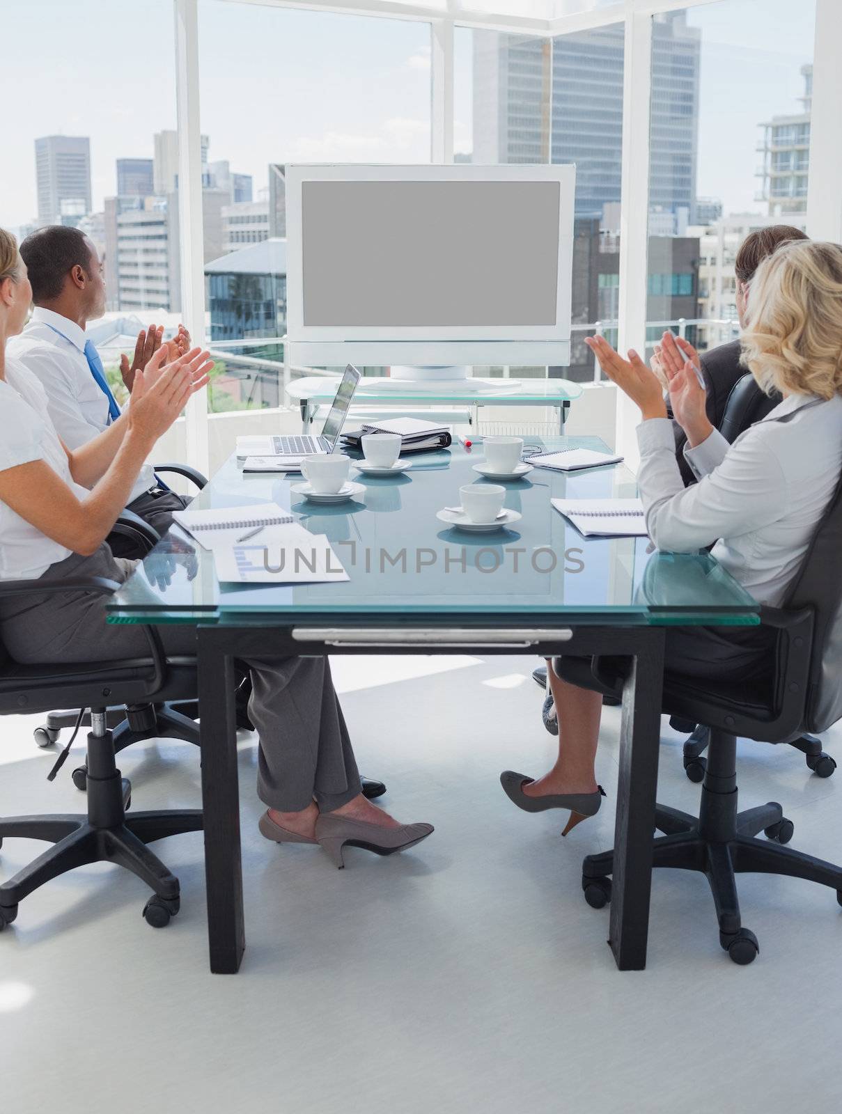 Business people applauding during a video conference while they are sat in the boardroom