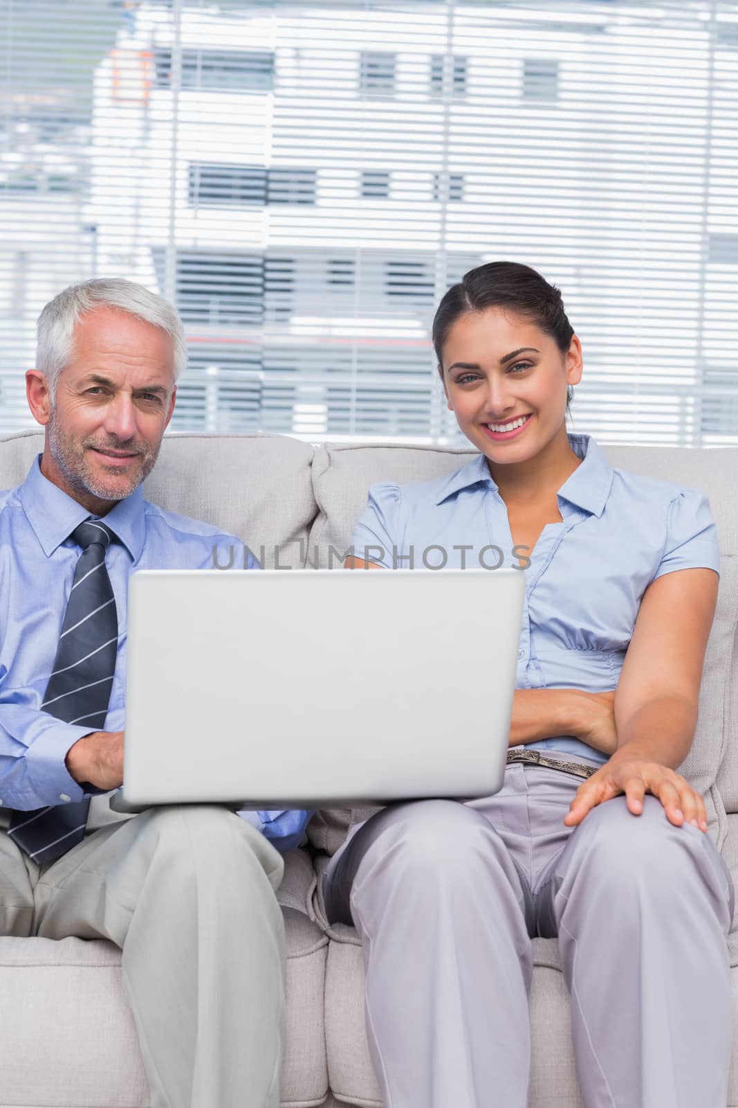 Business people with laptop smiling at camera sitting on couch in office staffroom
