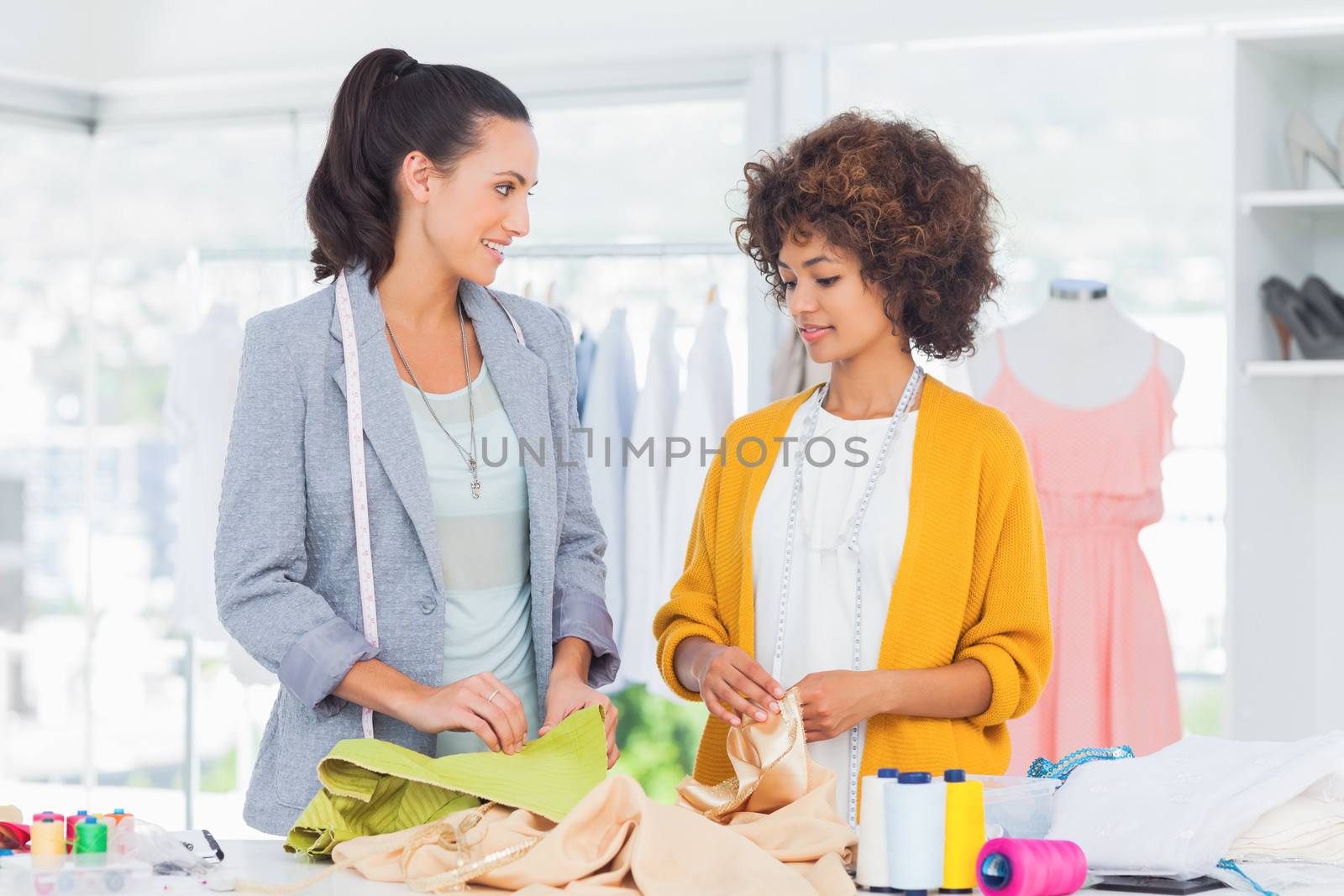 Two cheerful fashion designers touching textile in a creative office