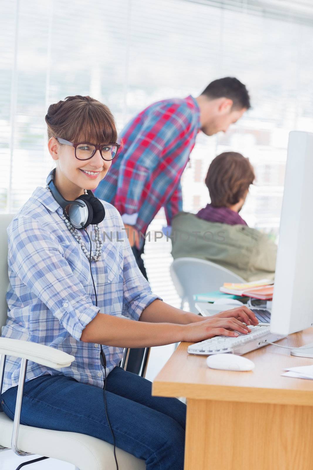 Pretty designer with headphone working on computer with colleagues discussing behind