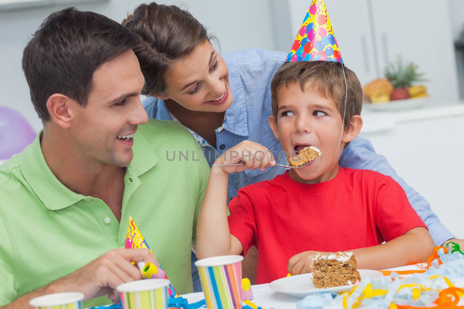 Little boy eating a birthday cake with parents during his birthday party
