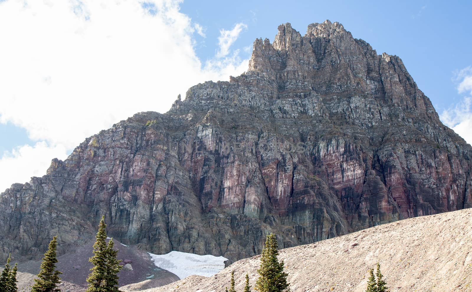 This image of Mount Reynolds at Glacier National Park shows purple rock face and remnants of a snow field.