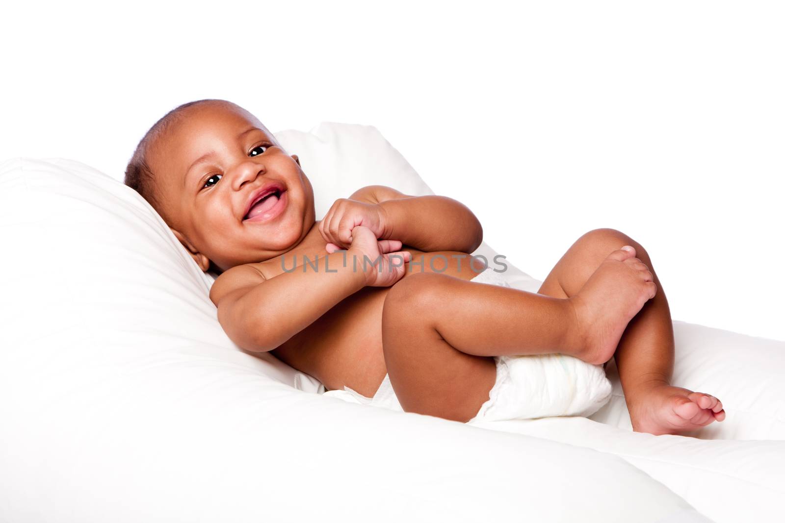Happy cute smiling laughing African baby infant laying wearing diapers on soft bed, isolated.