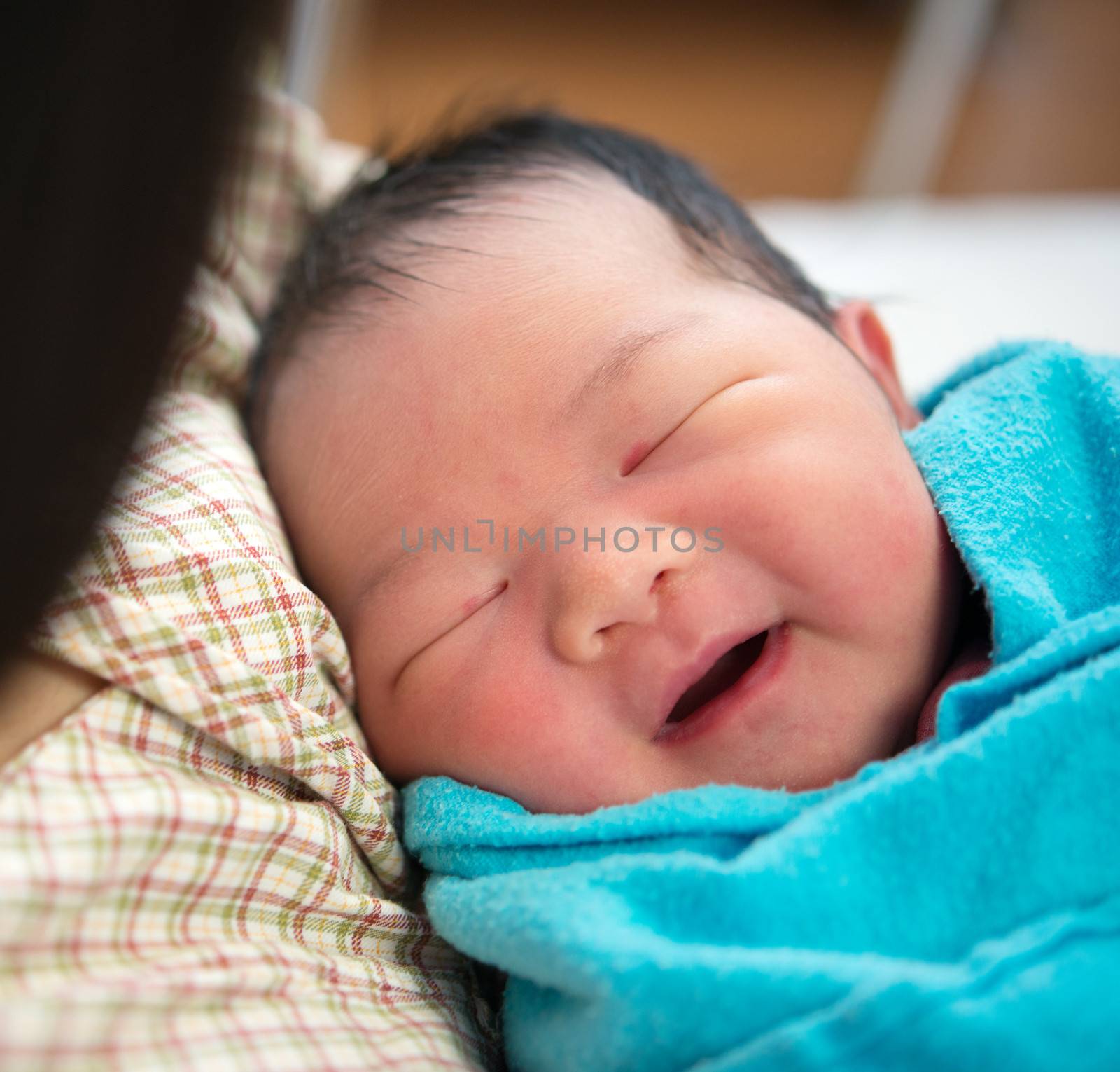 Newborn Asian baby girl smiling and fall asleep in mother's arms, inside hospital room