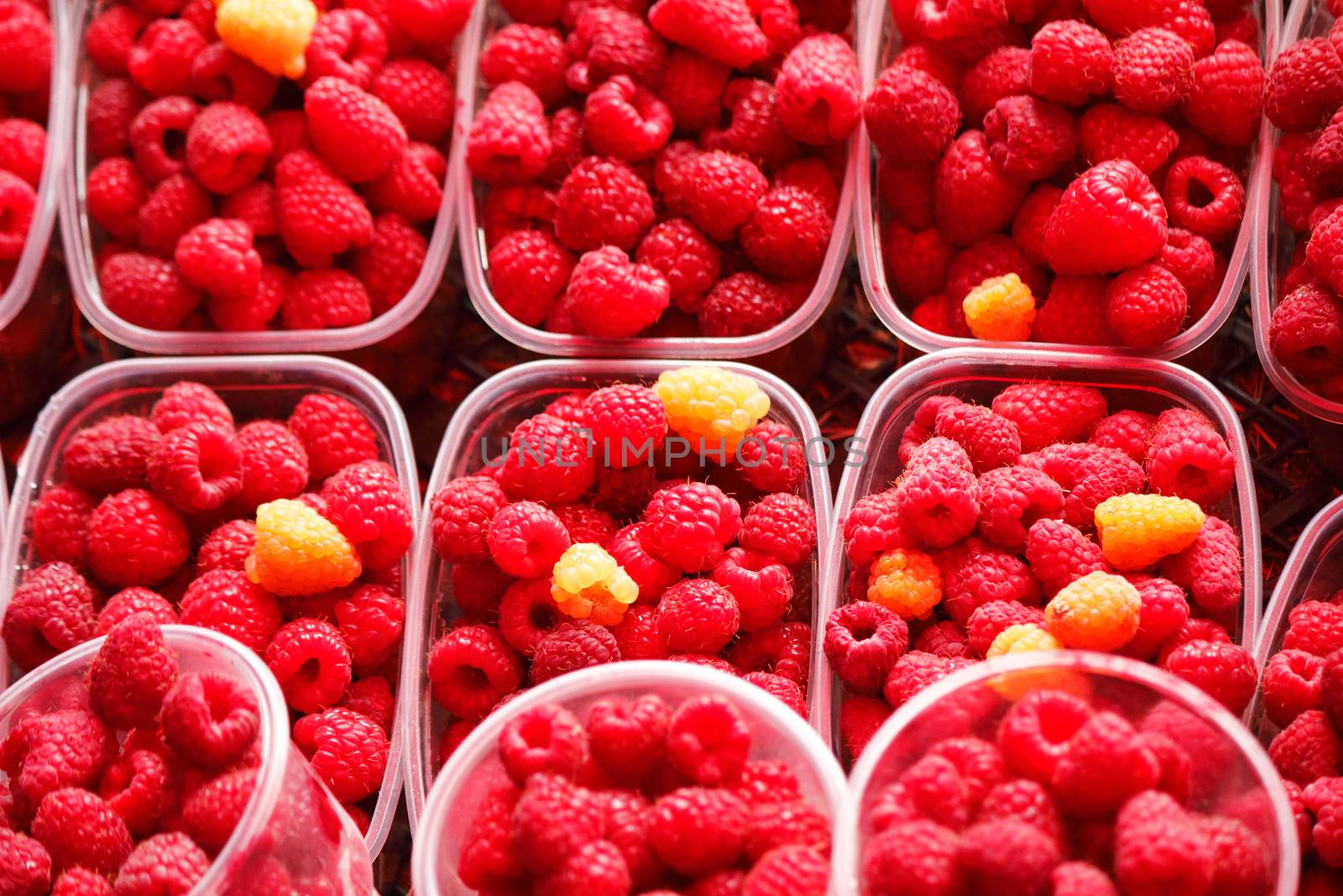 Ripe yellow and red raspberries in small containers for sale in the store.