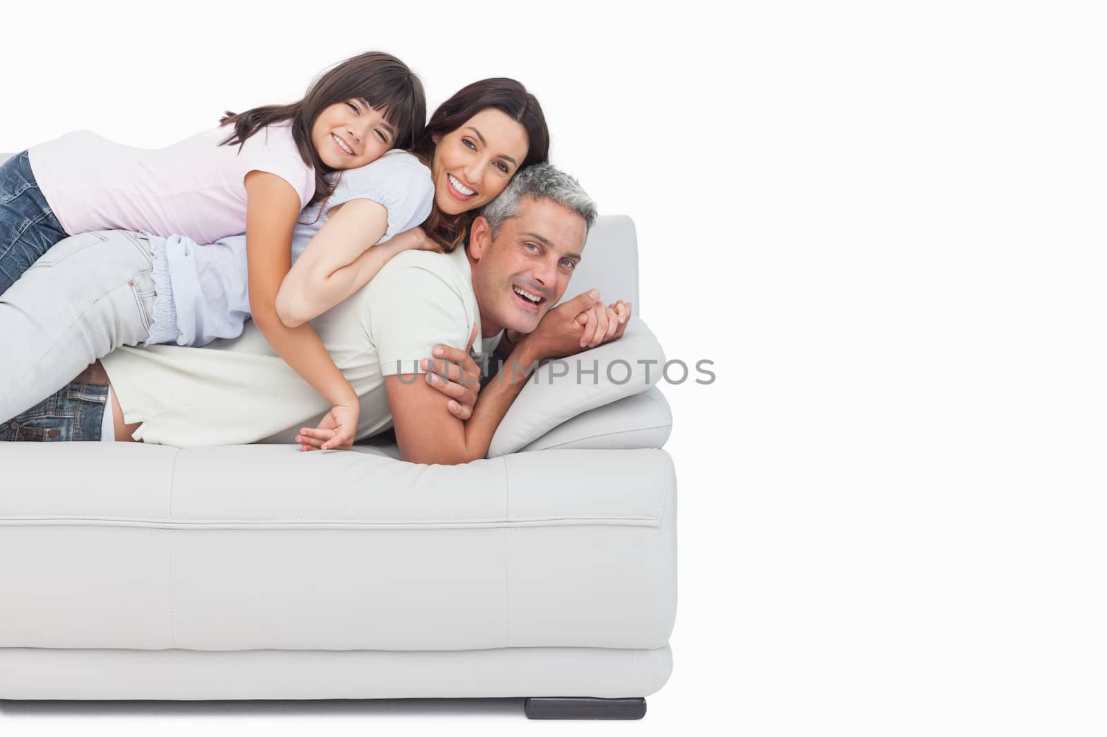 Smiling little girl lying on her parents on sofa  by Wavebreakmedia