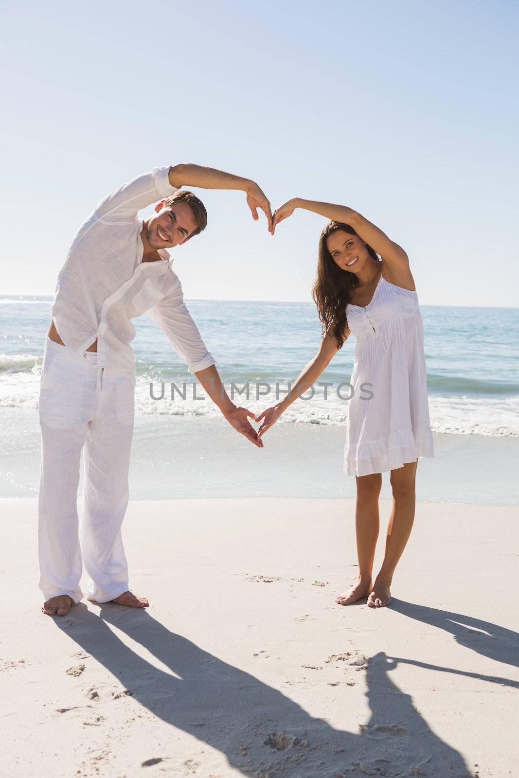 Romantic couple forming heart shape with arms at the beach