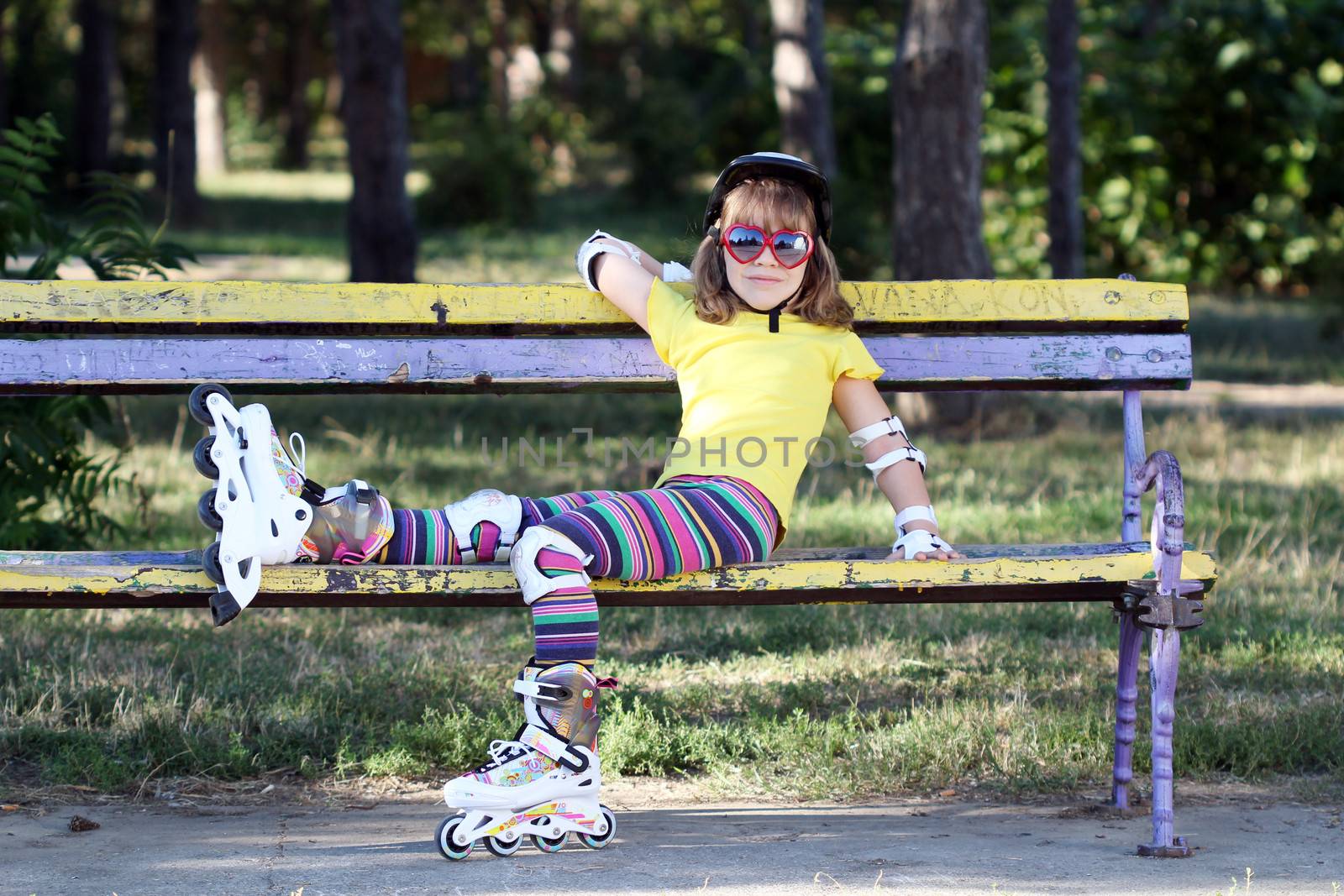 little girl with roller skates and helmet sitting on bench