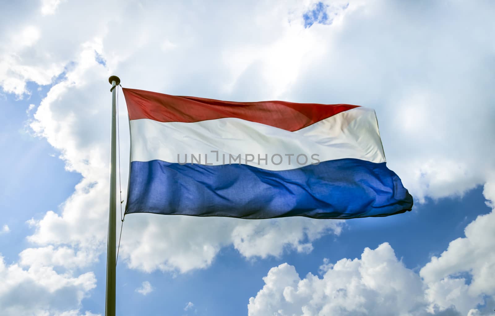 Waving flag of The Netherlands on the flagpole against cloudy blue sky