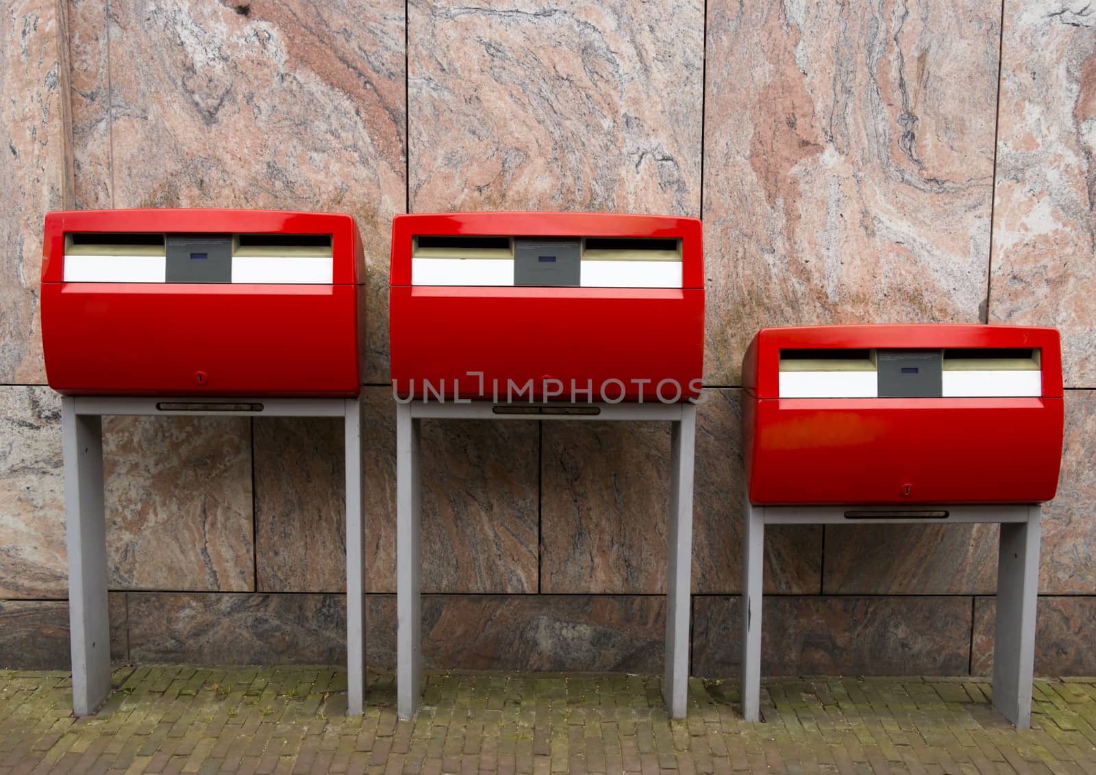Three red public mailboxes with two slots, common in the Netherlands