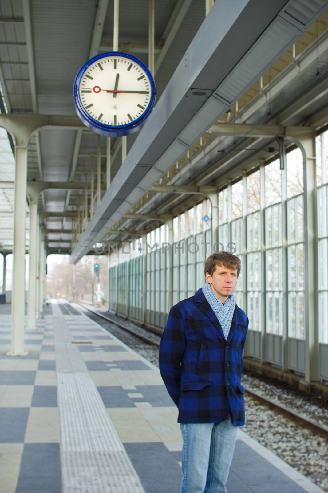 A man waiting for a train under a clock by Tetyana