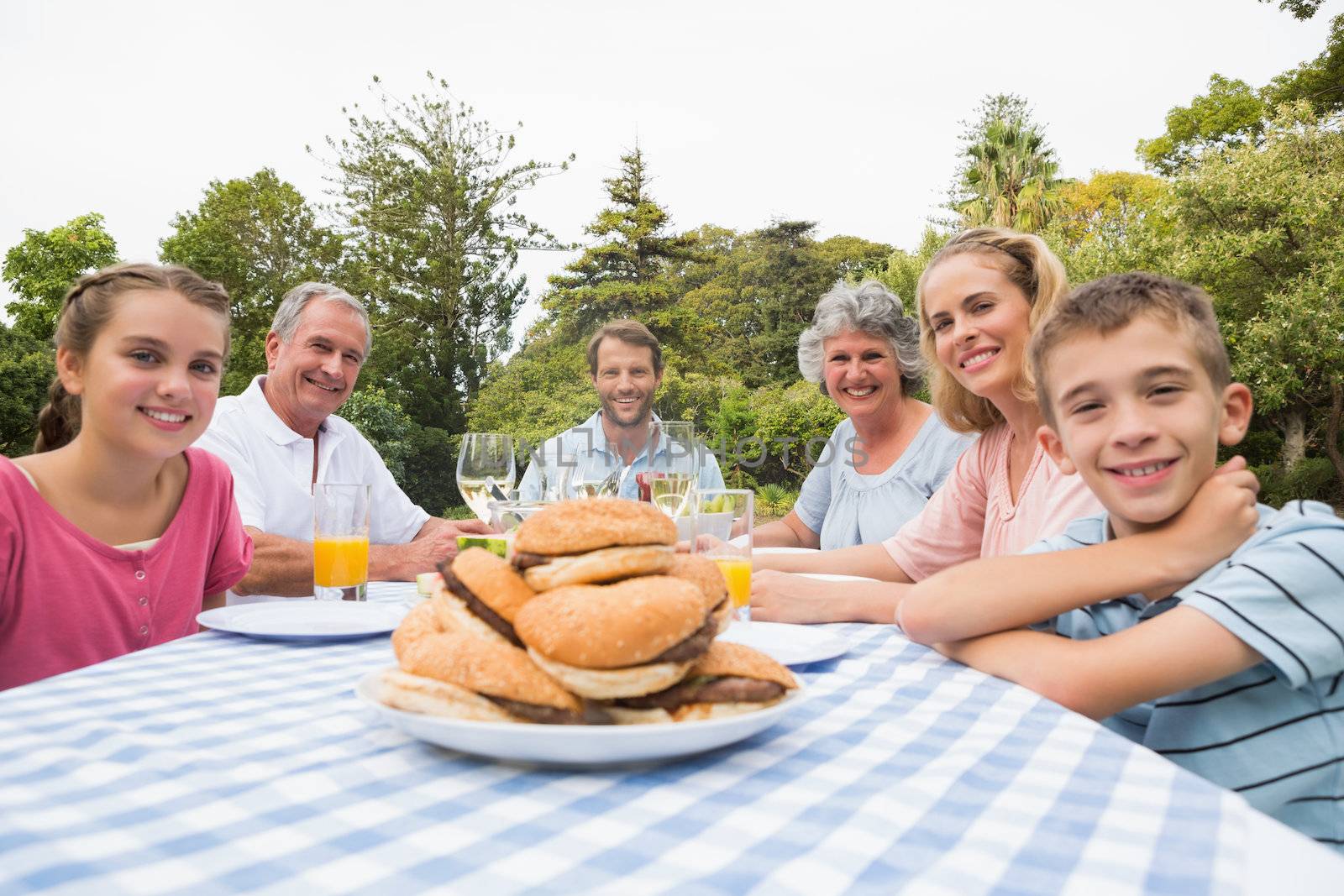 Extended family eating outdoors at picnic table smiling at camera