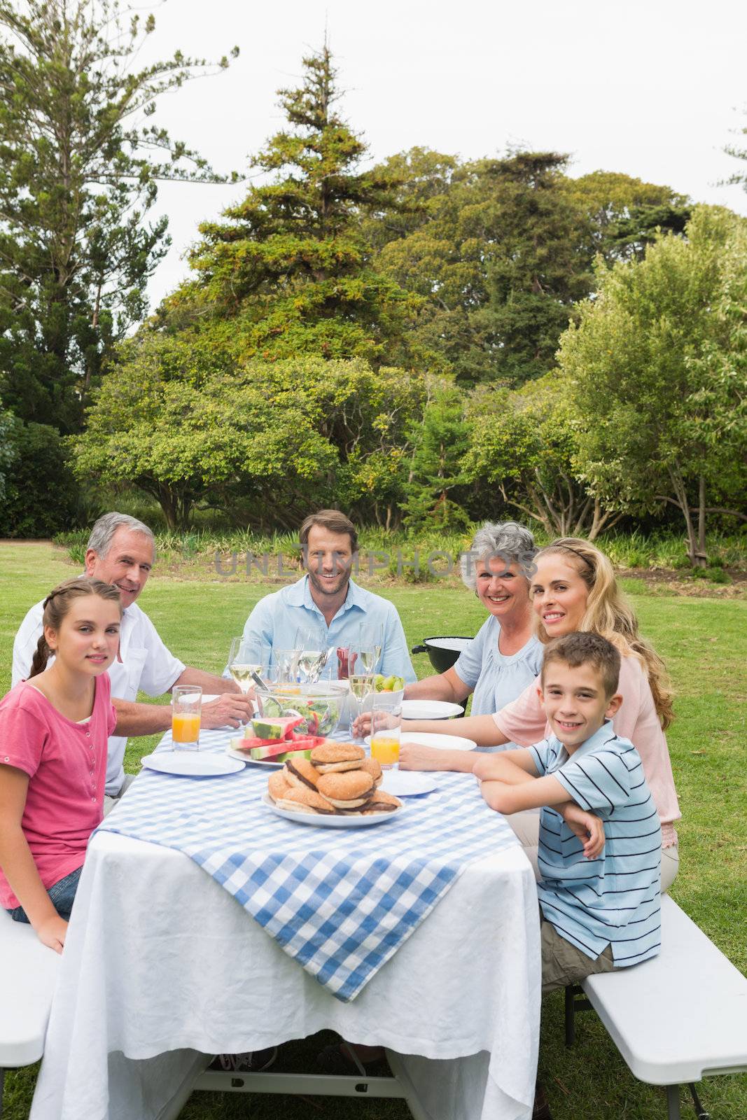 Multi generation family at picnic table having dinner outside smiling at camera