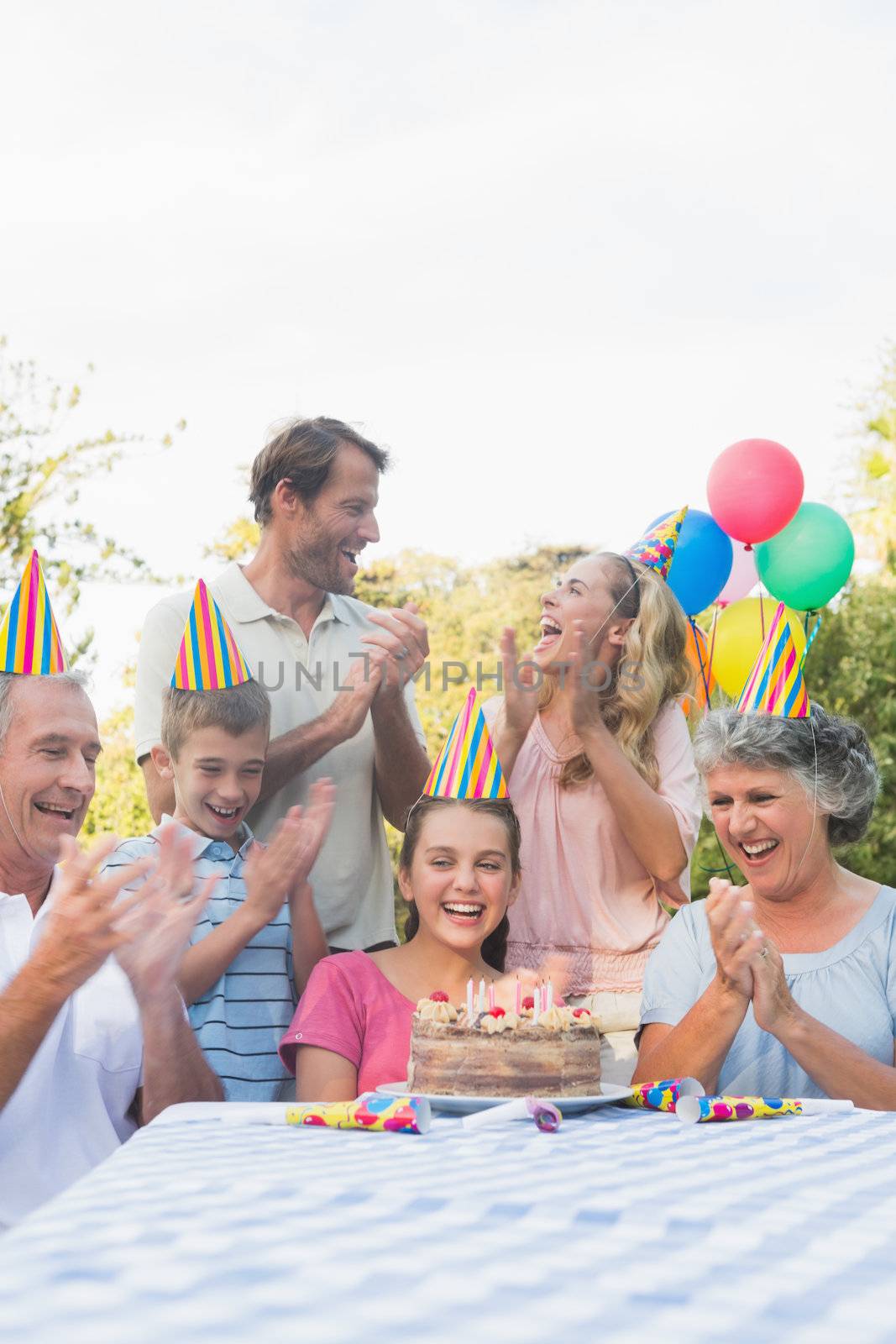 Cheerful extended family clapping for little girls birthday outside at picnic table