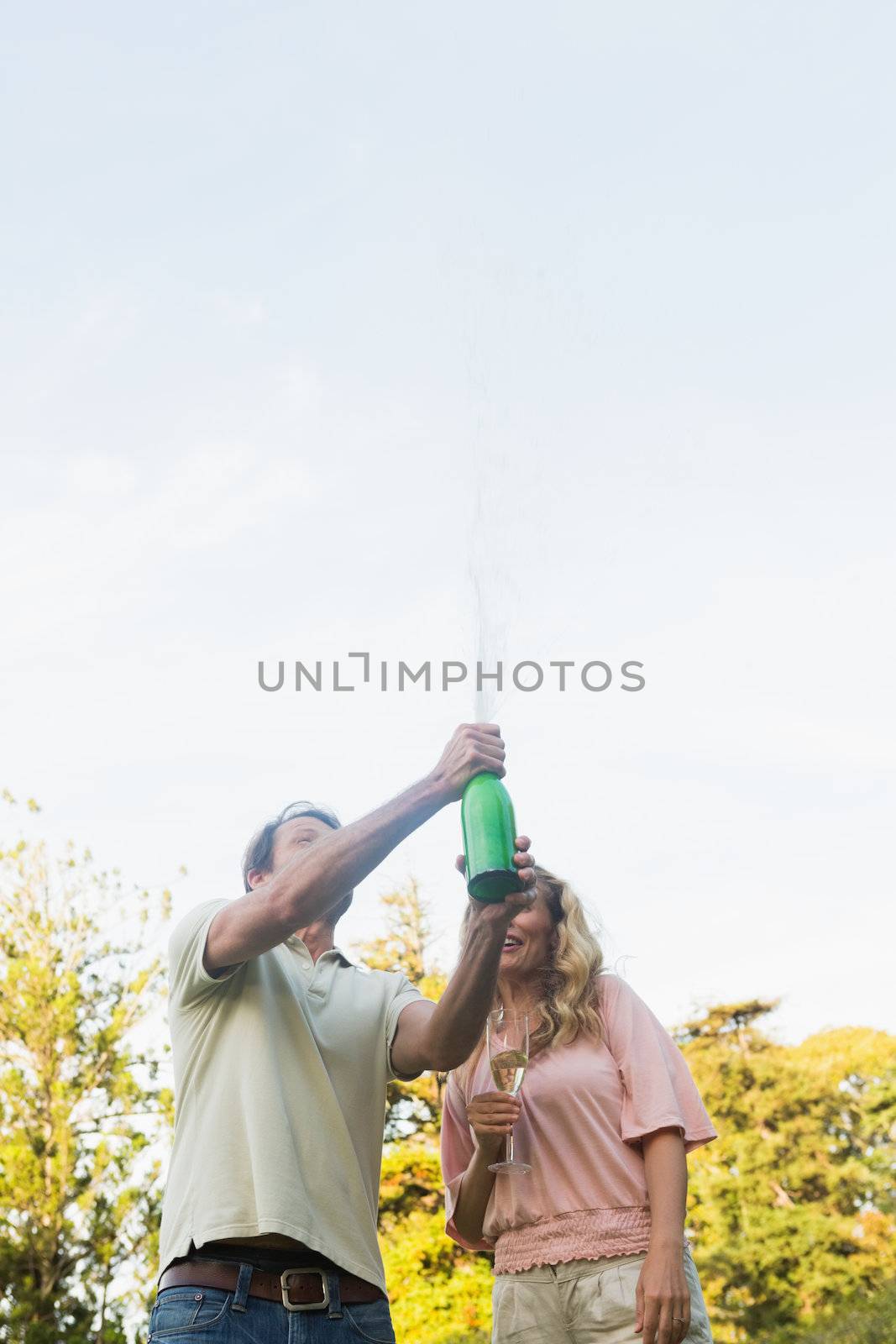 Man spraying bottle of champagne with blonde partner by Wavebreakmedia