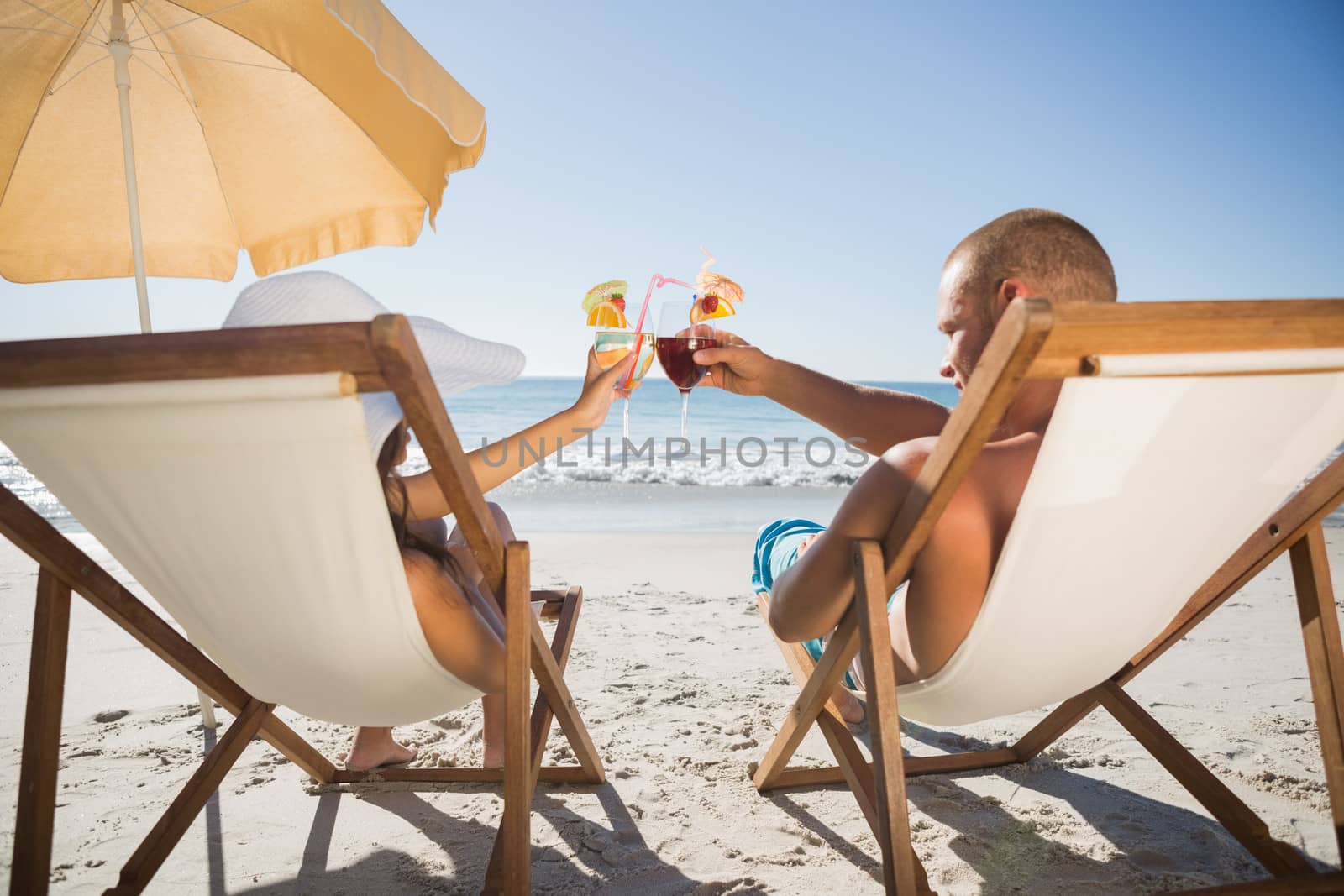 Happy couple clinking their glasses while relaxing on their deck chairs by Wavebreakmedia