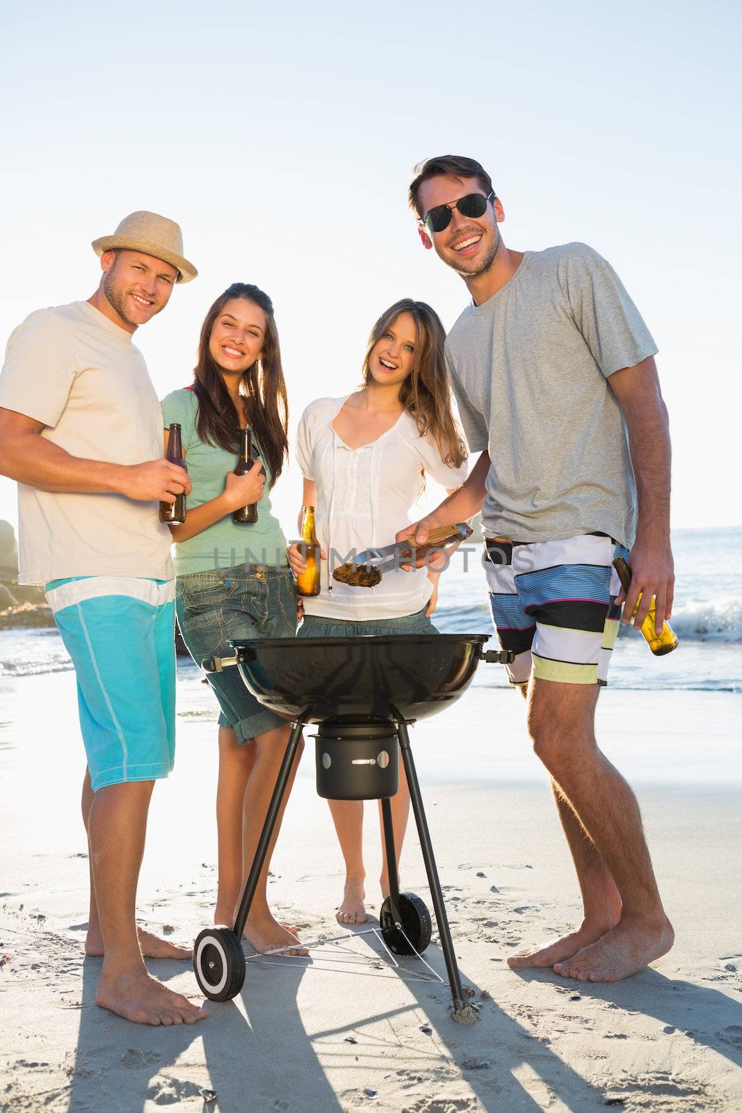 Happy friends on the beach looking at camera while having barbecue together